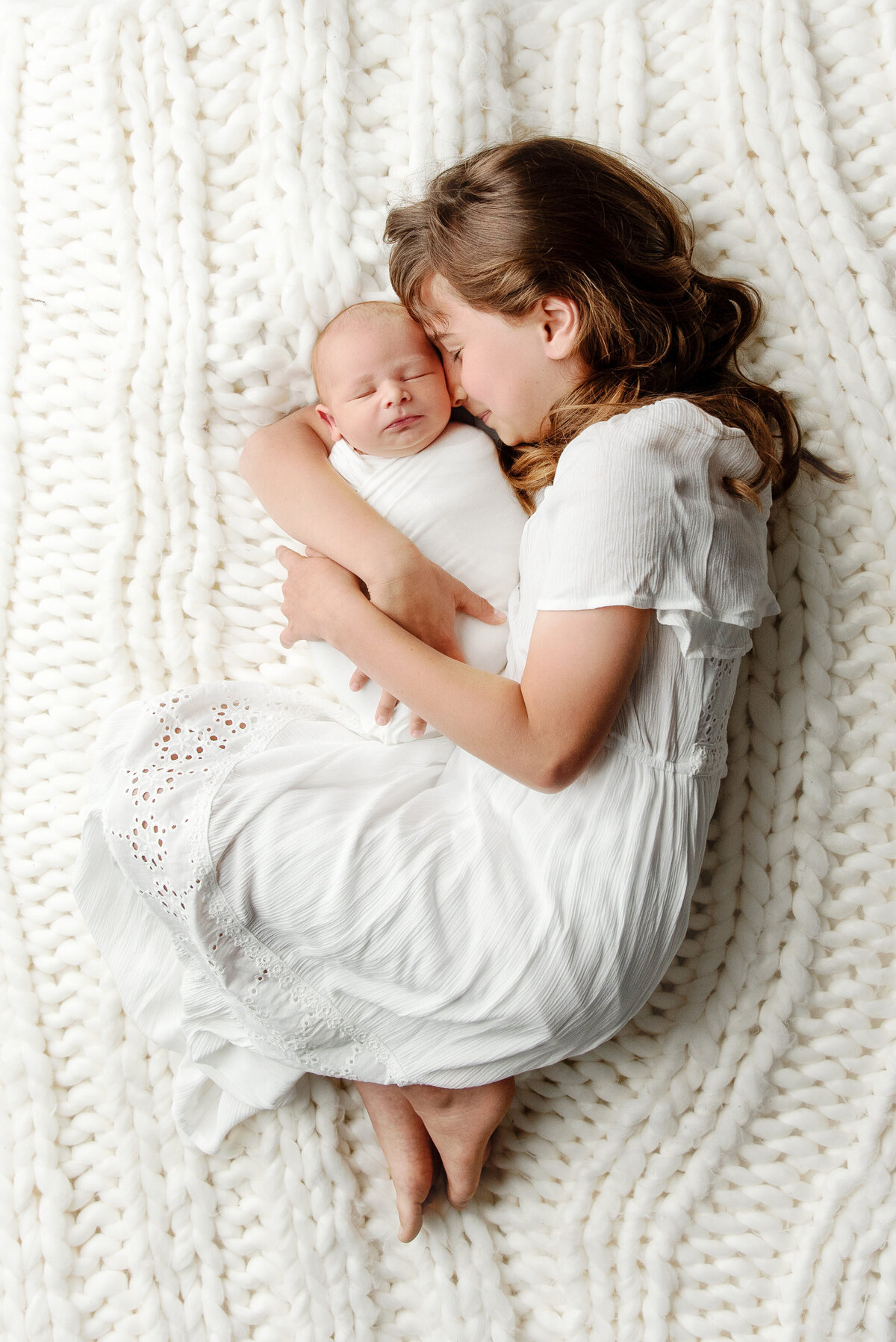 st-louis-newborn-photographer-baby-snuggled-by-big-sister-in-monocromatic-white-outfits-on-white-knitted-blanket