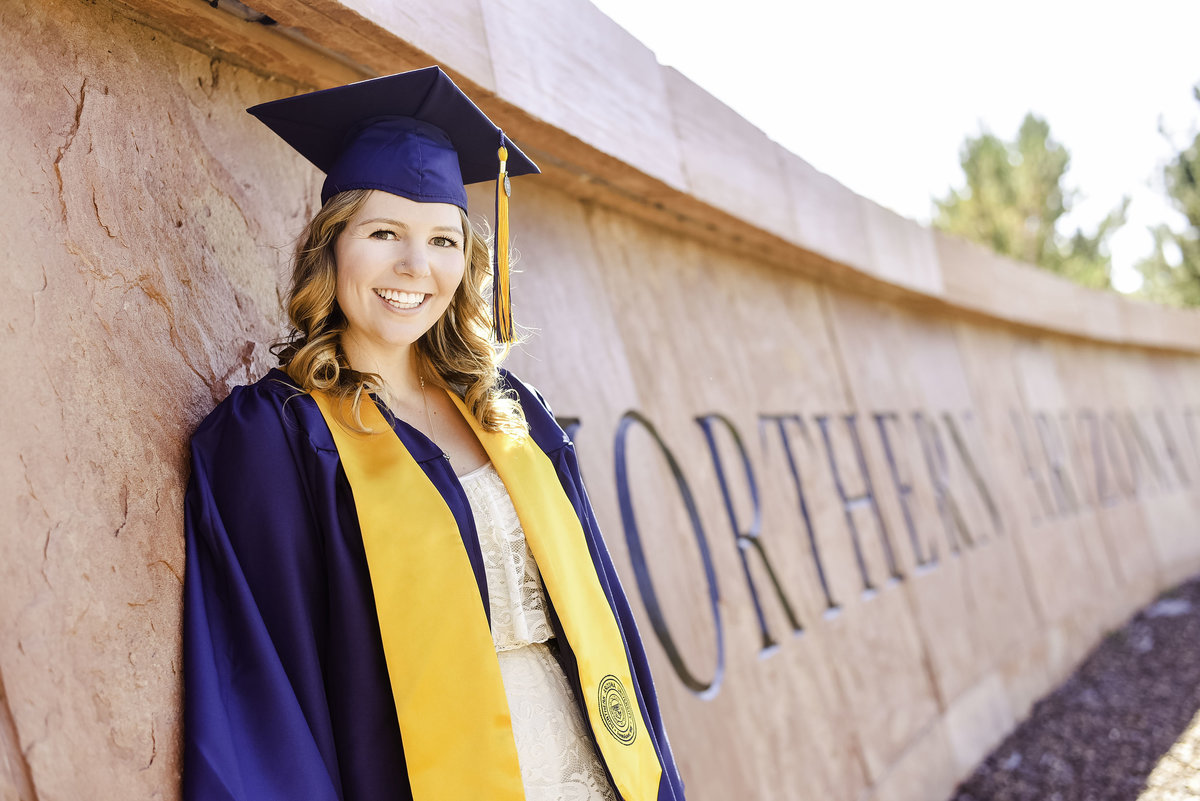 NAU senior wearing cap and gown standing at sign south campus Northern Arizona University Flagstaff