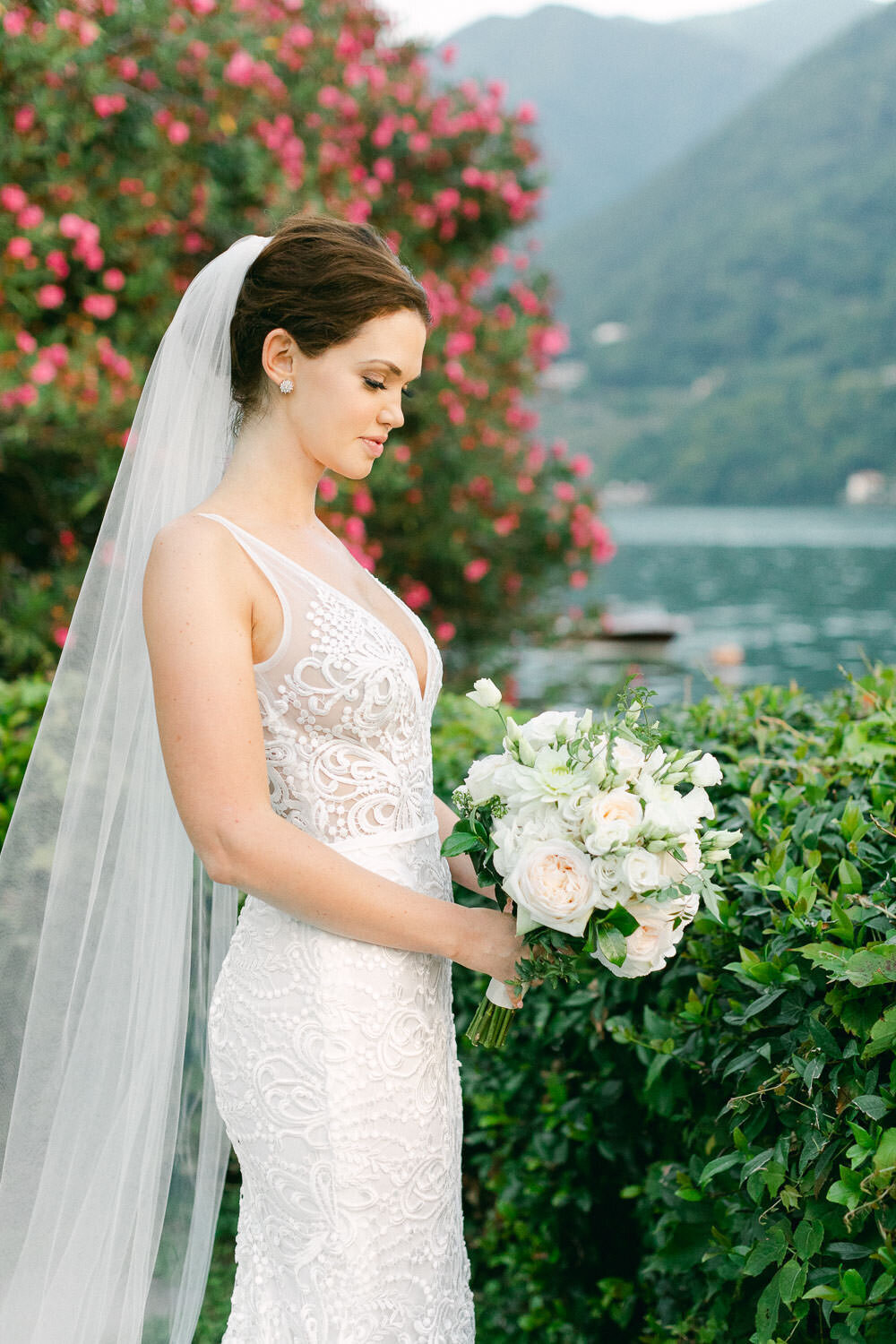Bride in white lace bridal dress and veil holding white floral bouquet by Lake Como Wedding Italy