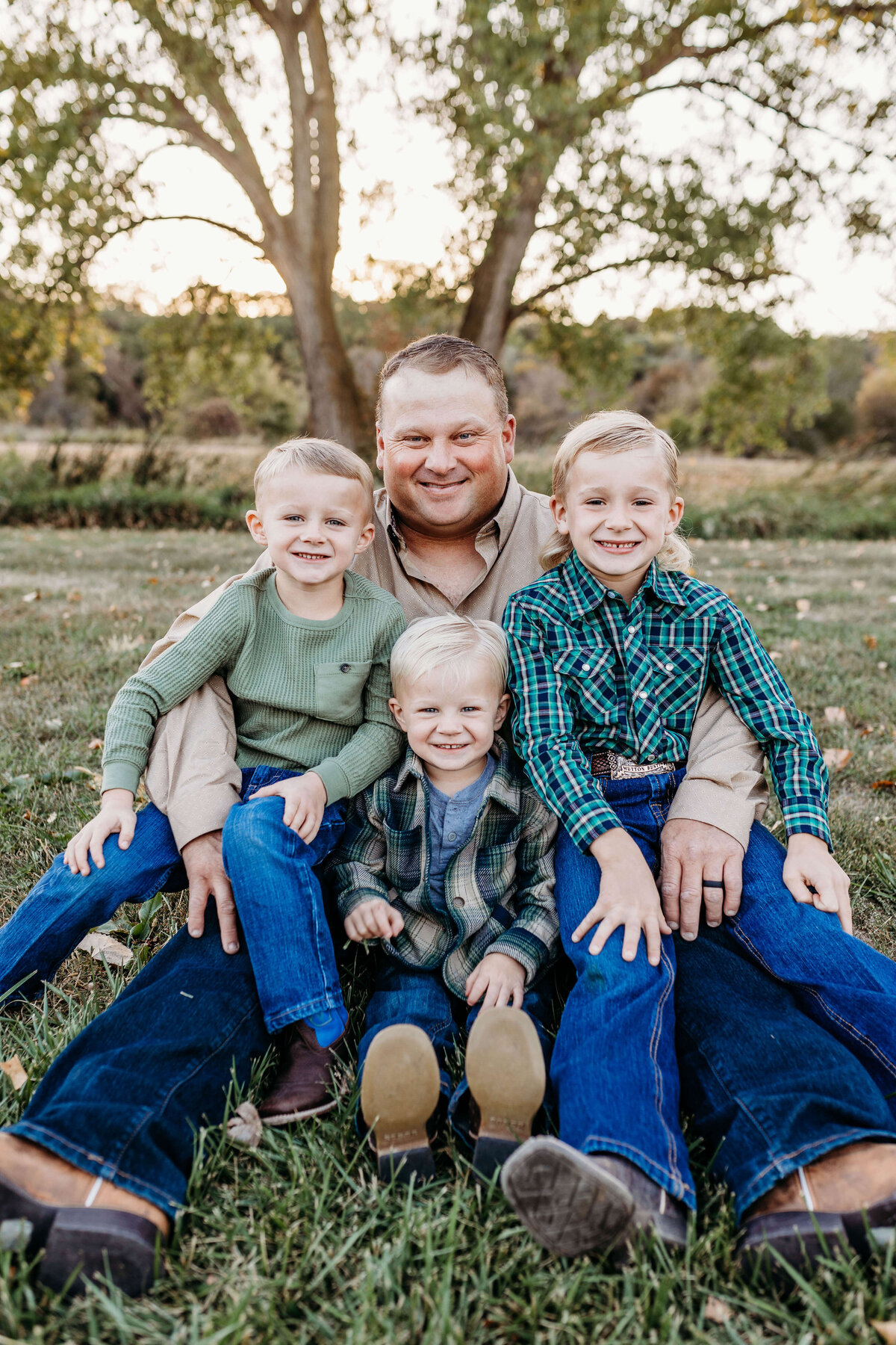 Dad is sitting with his 3 blonde boys in central nebraska.