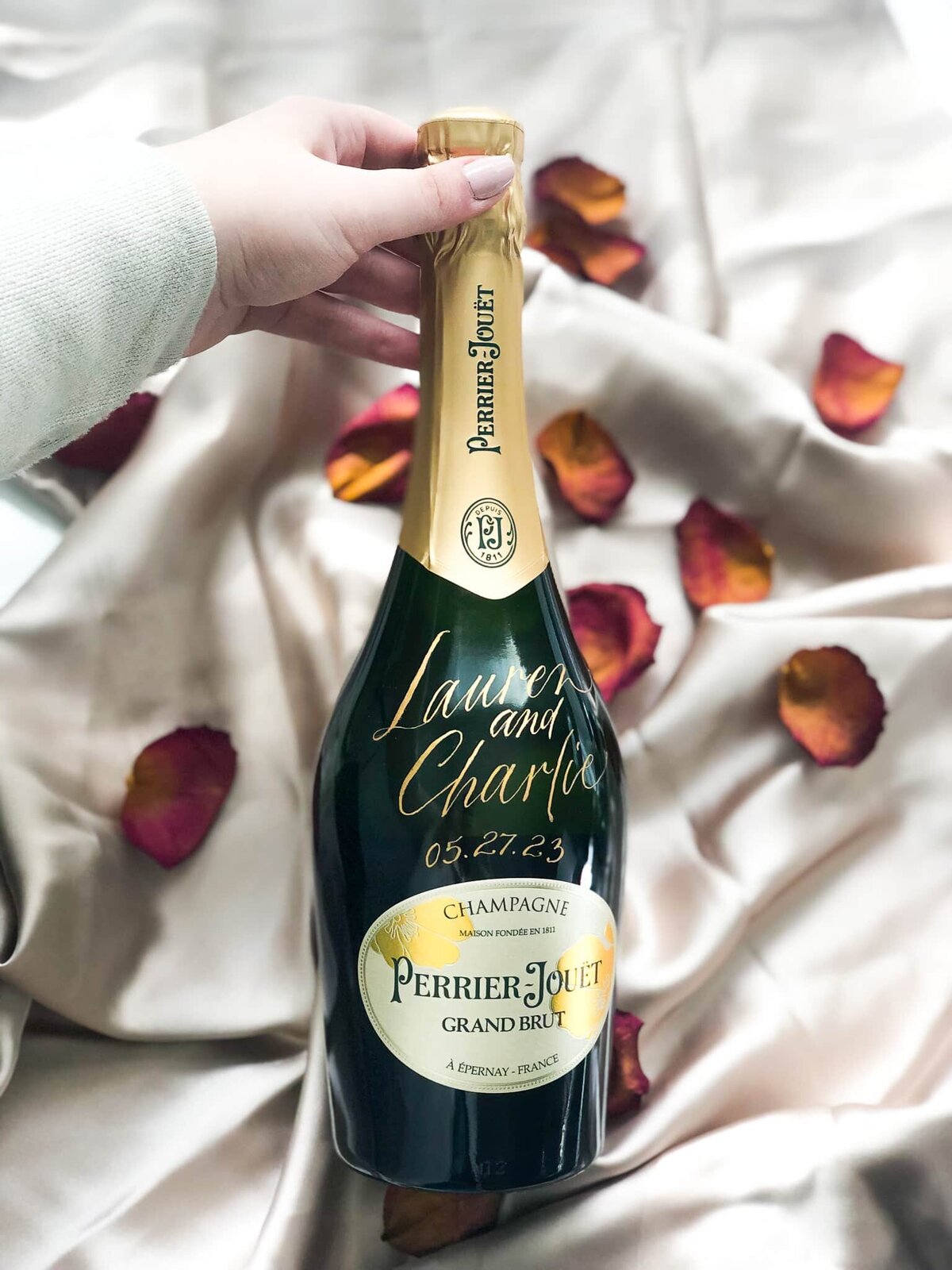 calligraphy champagne bottle against a silk background surrounded by dried roses