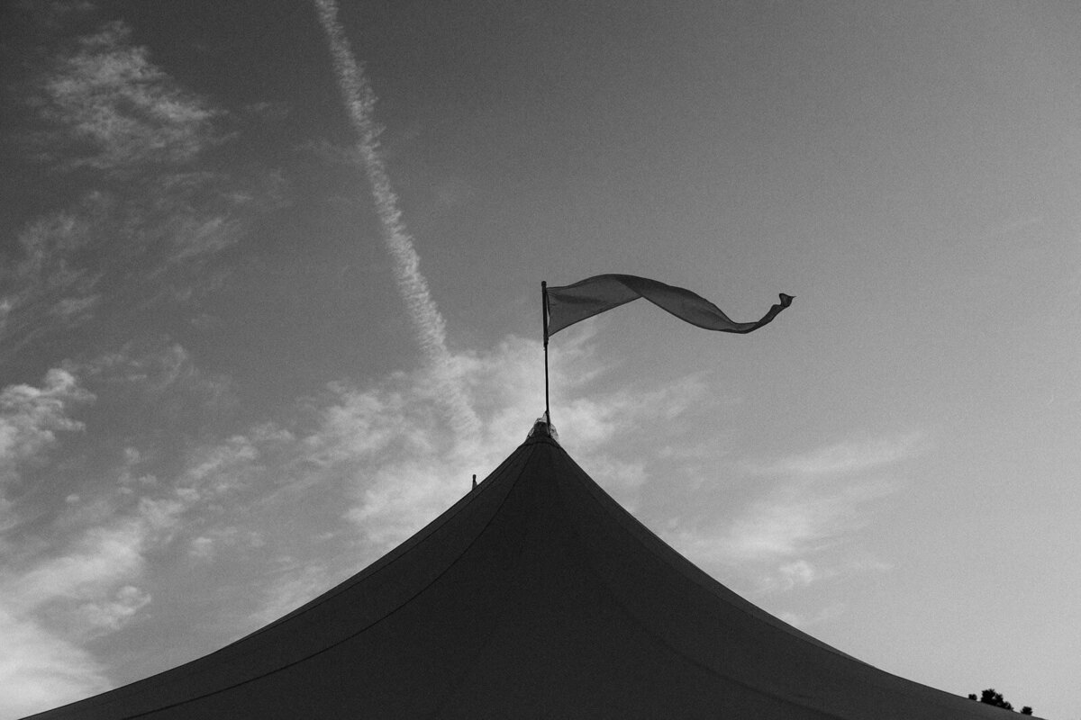 Black and white photo of the top portion of the Cape Cod Summer Tent, with a flag on top; the sky is on the background.