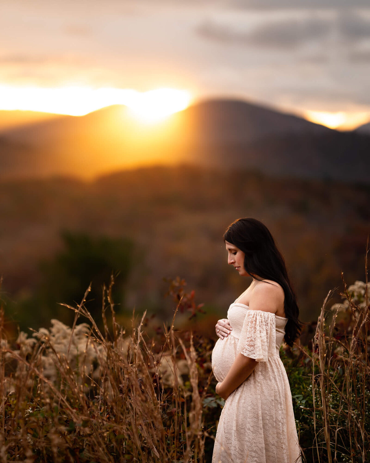 A beautiful mama to be holds her baby bump as the sun sets behind her