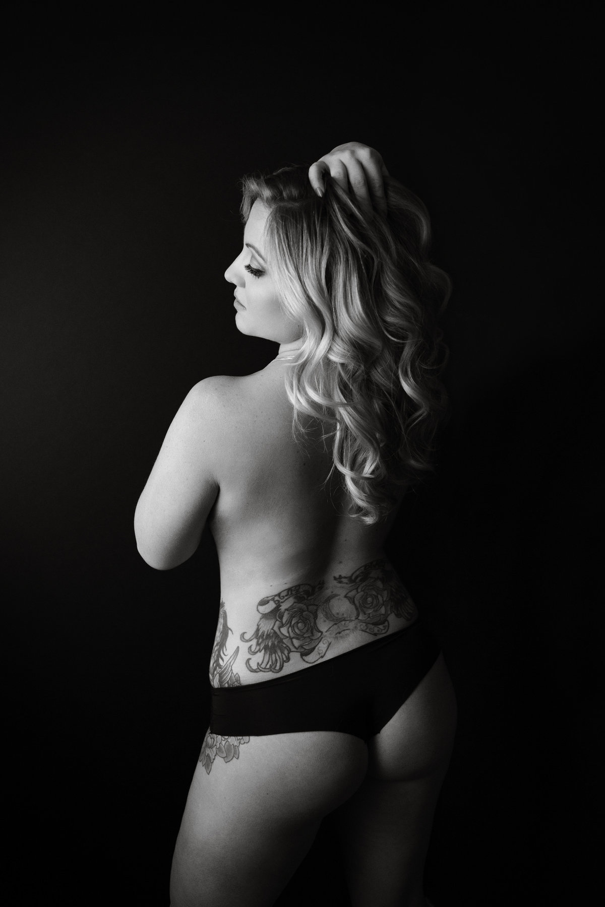 Woman poses against black background with tattoos and black underwear