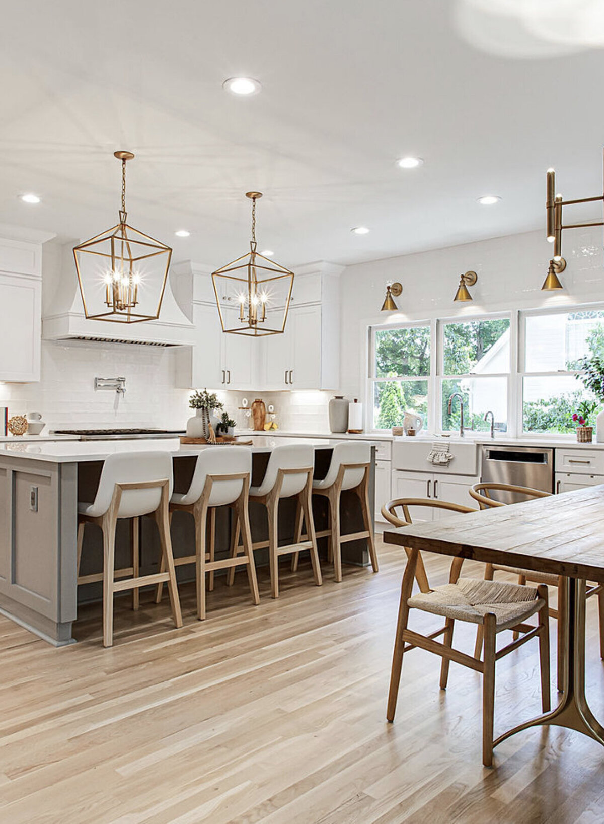 Bright, modern kitchen with white cabinets, gold light fixtures, a large island with bar stools, and a wooden dining table with chairs.