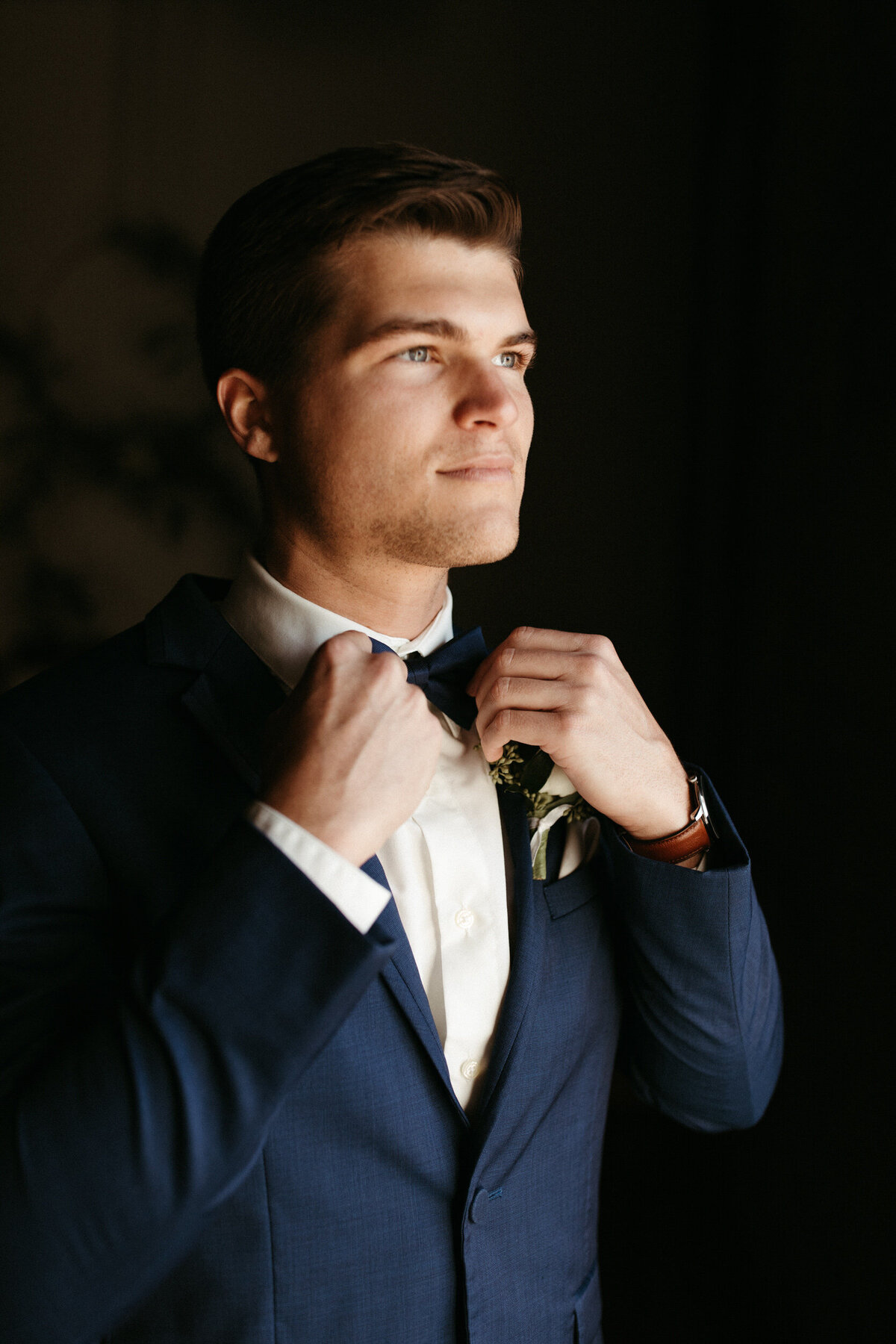 Groom in blue suit getting ready in front of window on his wedding day