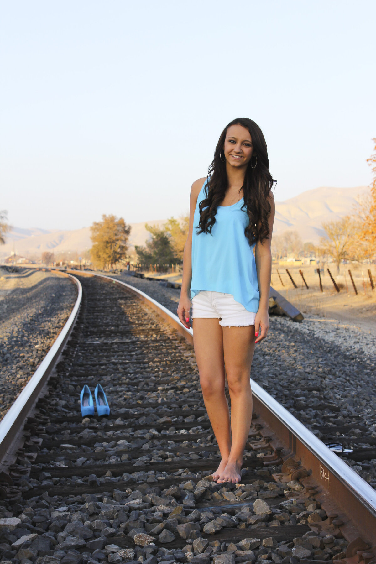 Lady on Railroad tracks  with glowing light of sunset beaming down golden light with blue high heal shoes in background