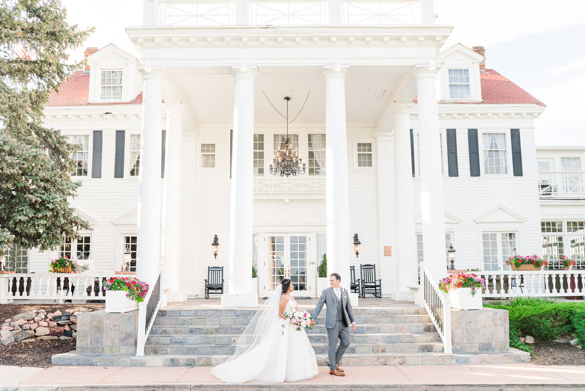 Wedding couple walking in front of a large white manor house.