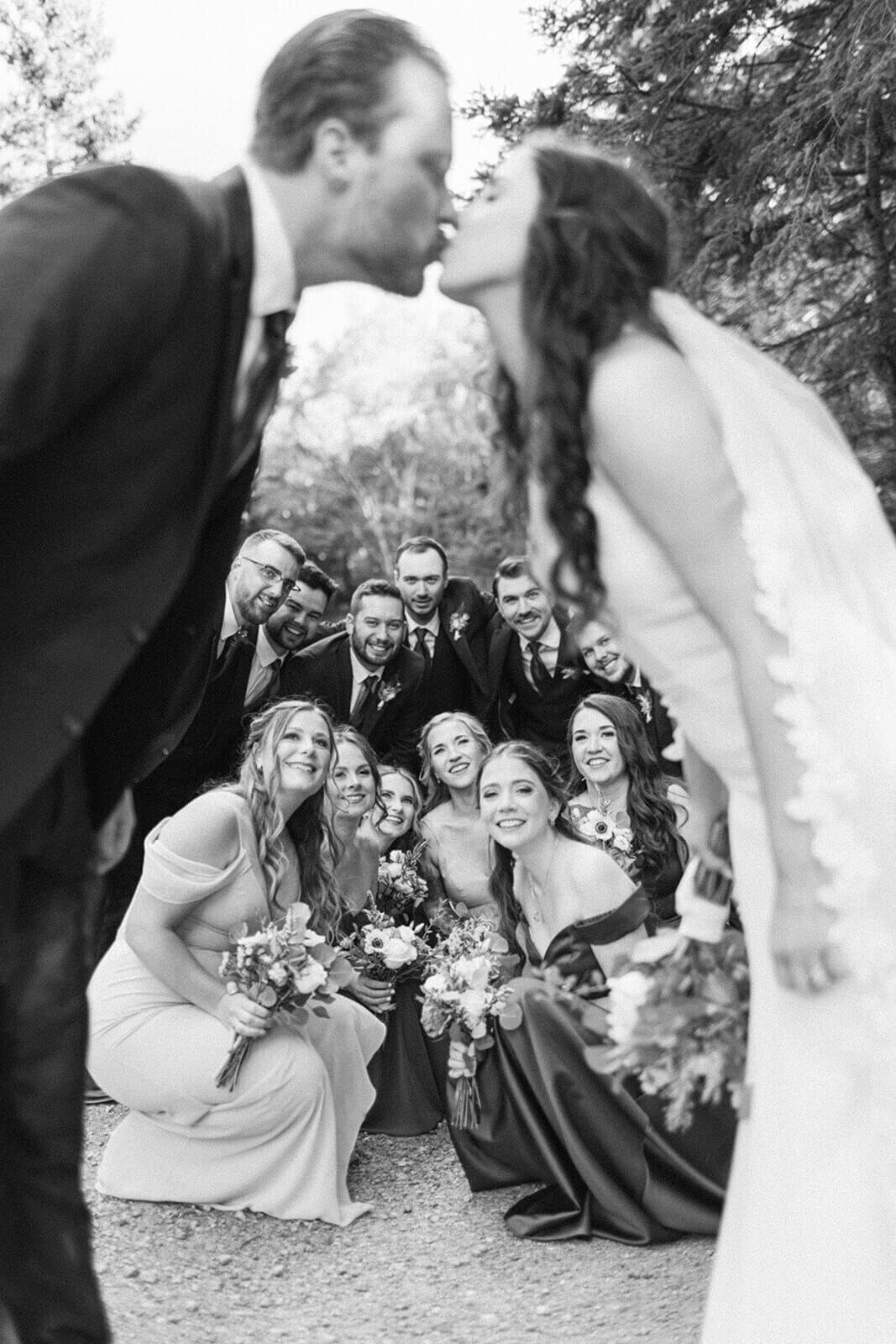 groom-and-bride-kissing-infront-of-wedding-party