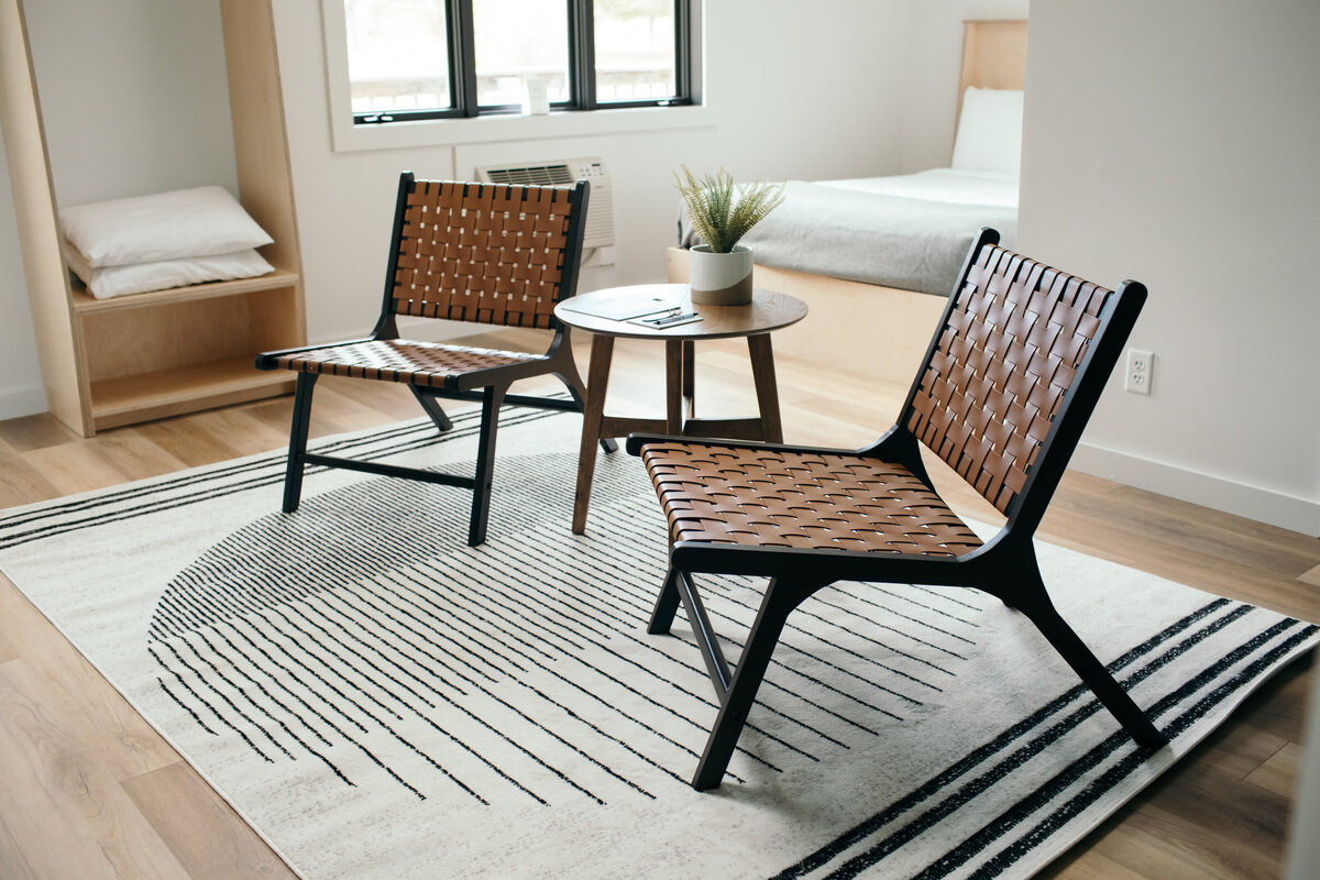 in the foreground twin chairs with brown leather latticework fram a small round table with a succulent on it.  In the background a hotel