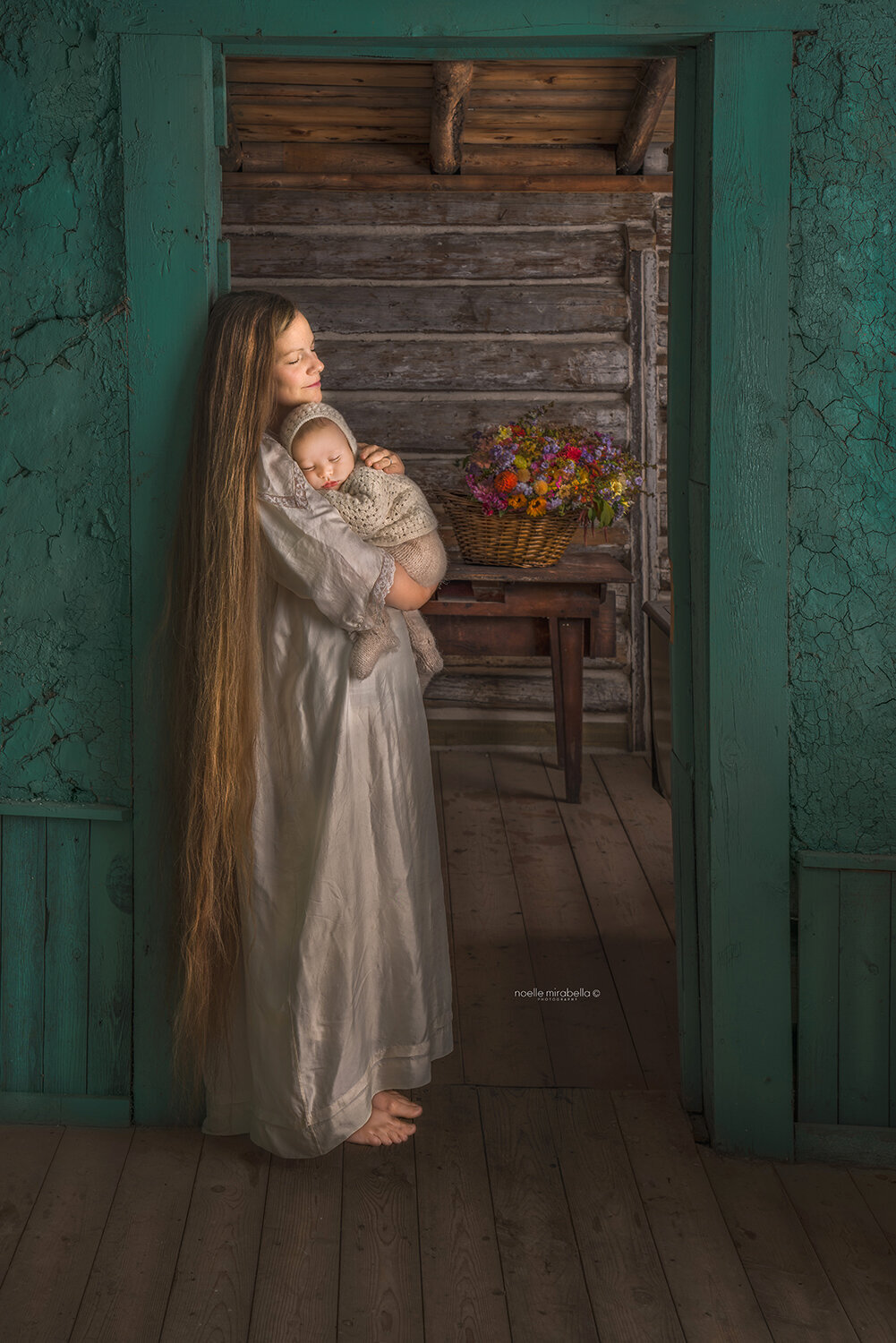 Woman/mother with floor length hair holding baby in doorway of 100-year-old house.