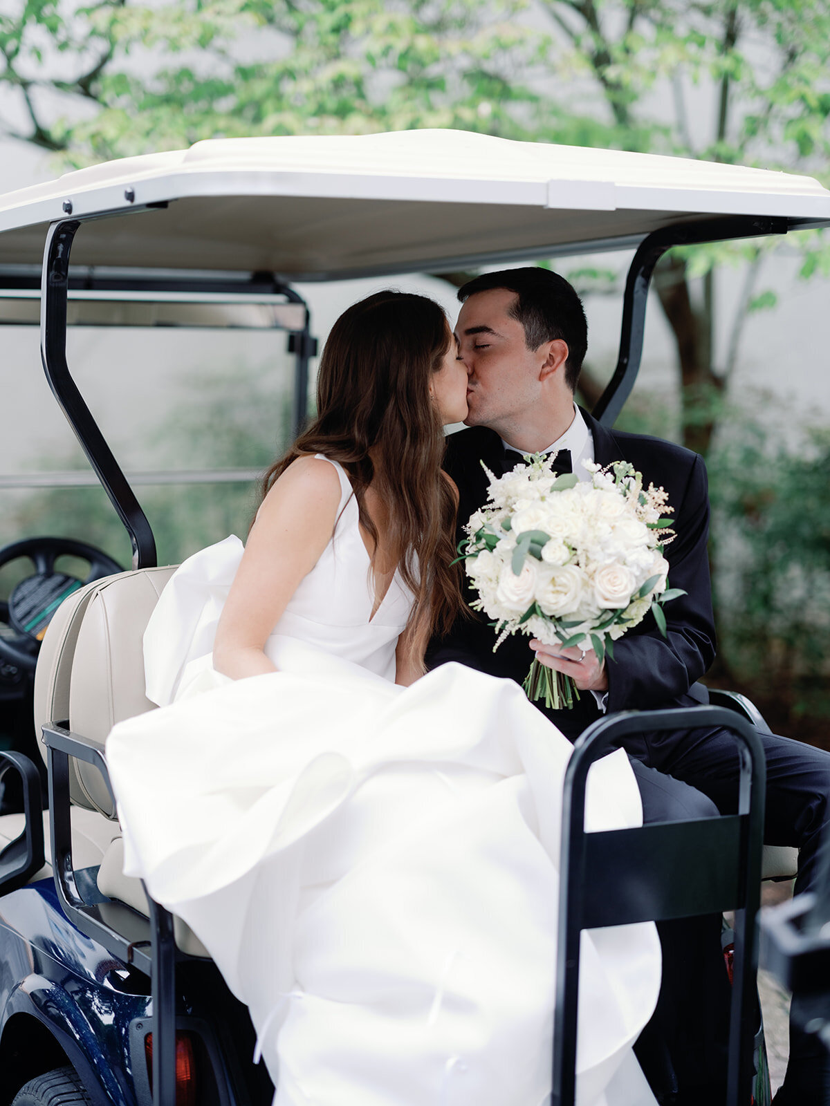 Bride and groom kiss while sitting on a golf cart