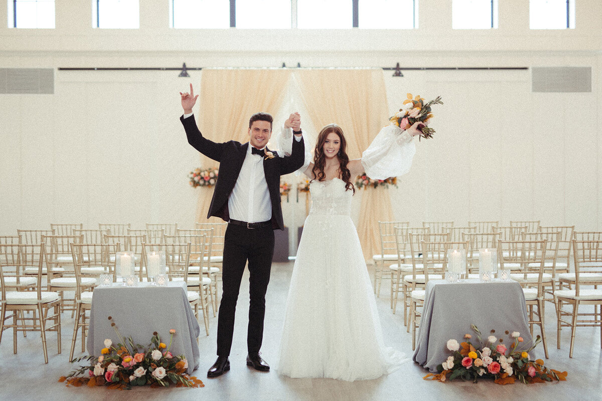 Bride and groom wearing a white wedding gown and black tuxedo pose in a bright and airy room.