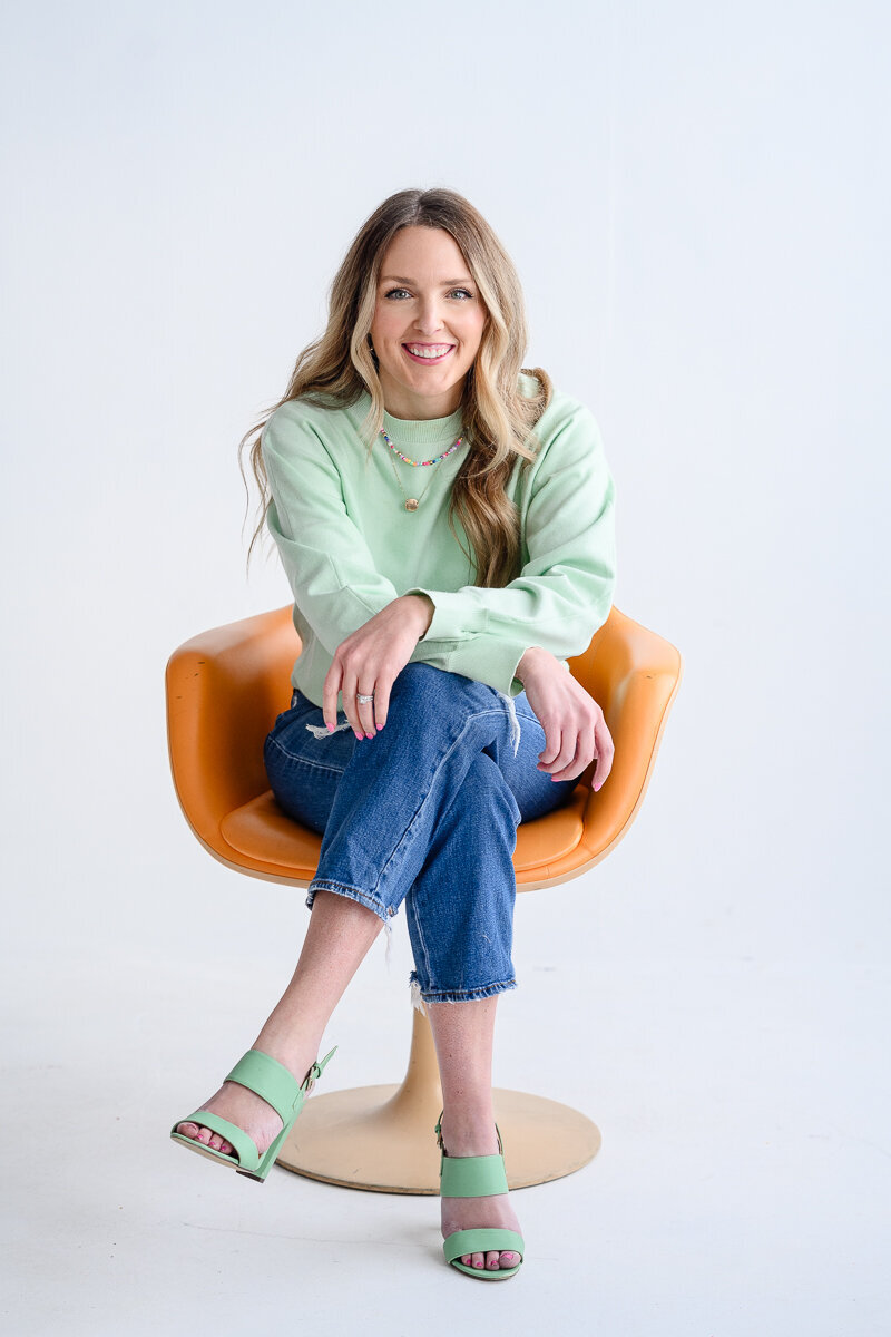 A Colorado creative watercolorist sits on an orange chair in a Denver photography studio for her Denver branding photos with LiLo Photography