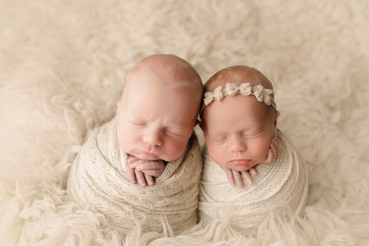 newborn boy and girl twins snuggled in cream blanket