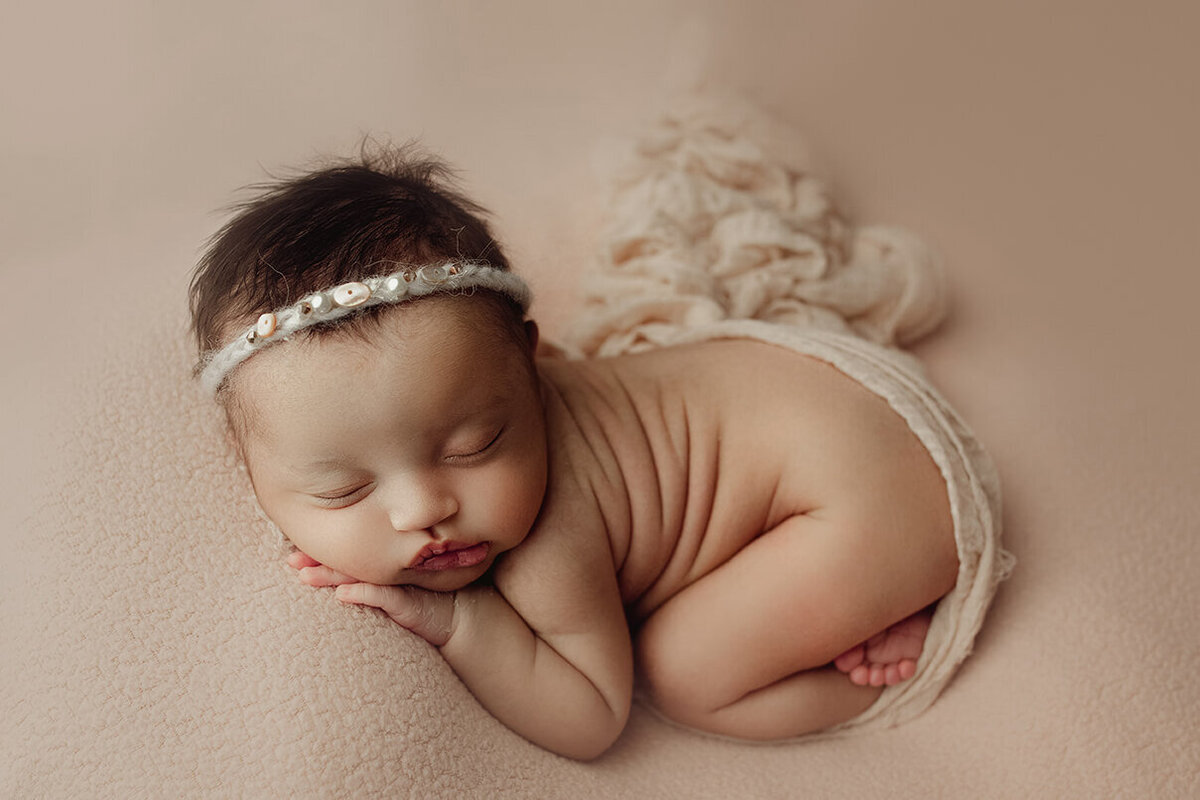 a newborn girl sleeping on her tummy on a tan backdrop