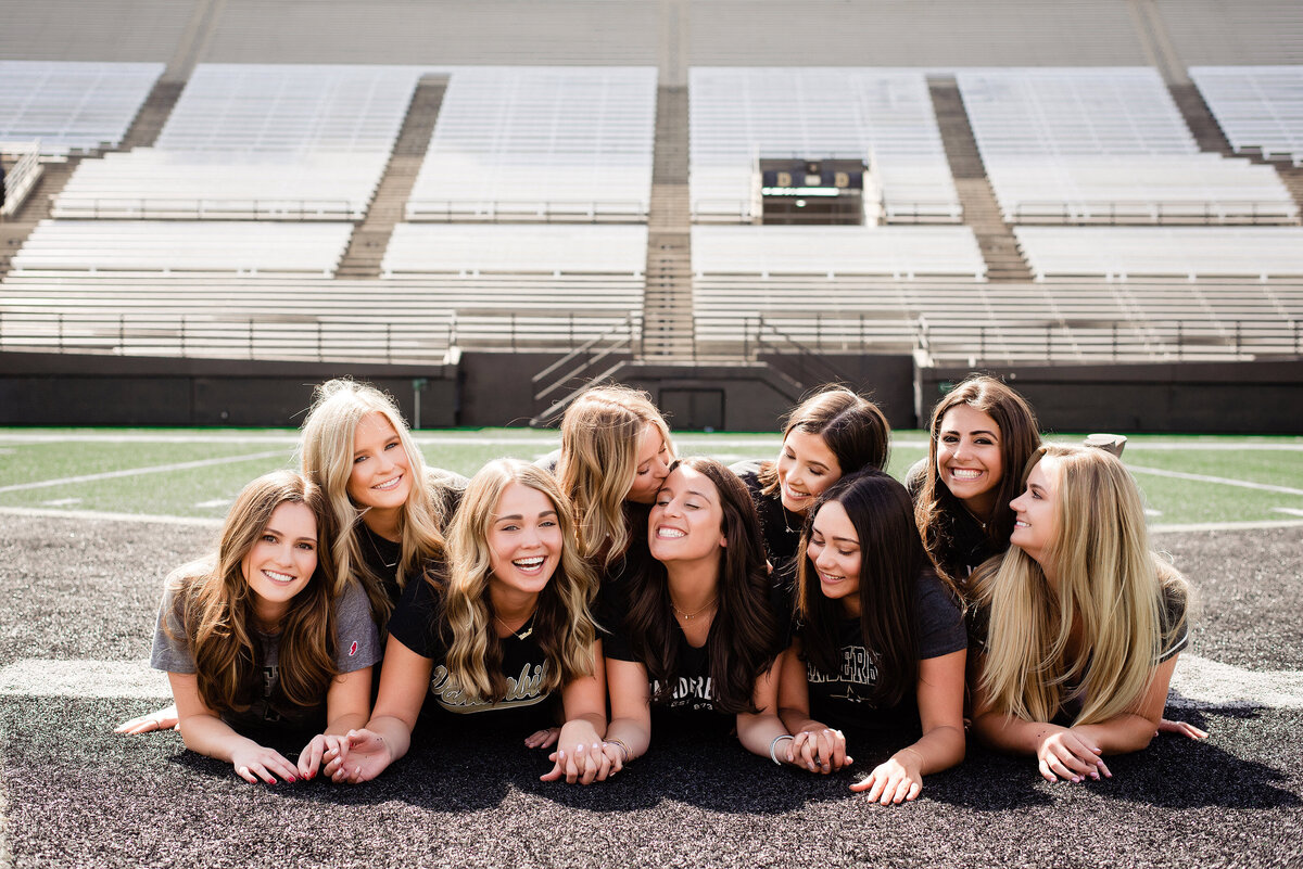 Girls laying on their stomachs on the football field, laughing together for senior graduation photos