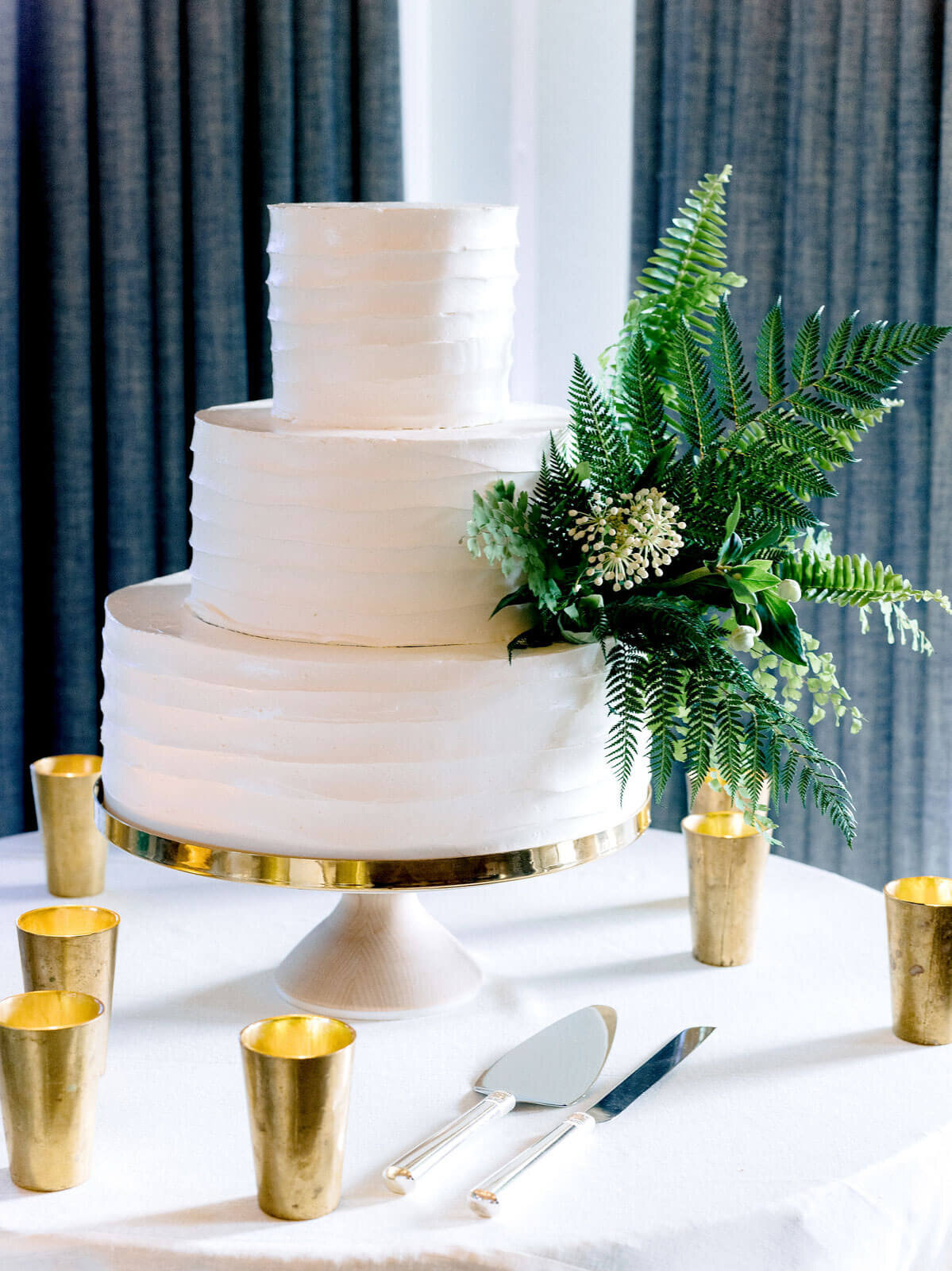 A three-layer, white wedding cake with green ferns, in Montage at Palmetto Bluff. Destination Wedding Image by Jenny Fu Studio