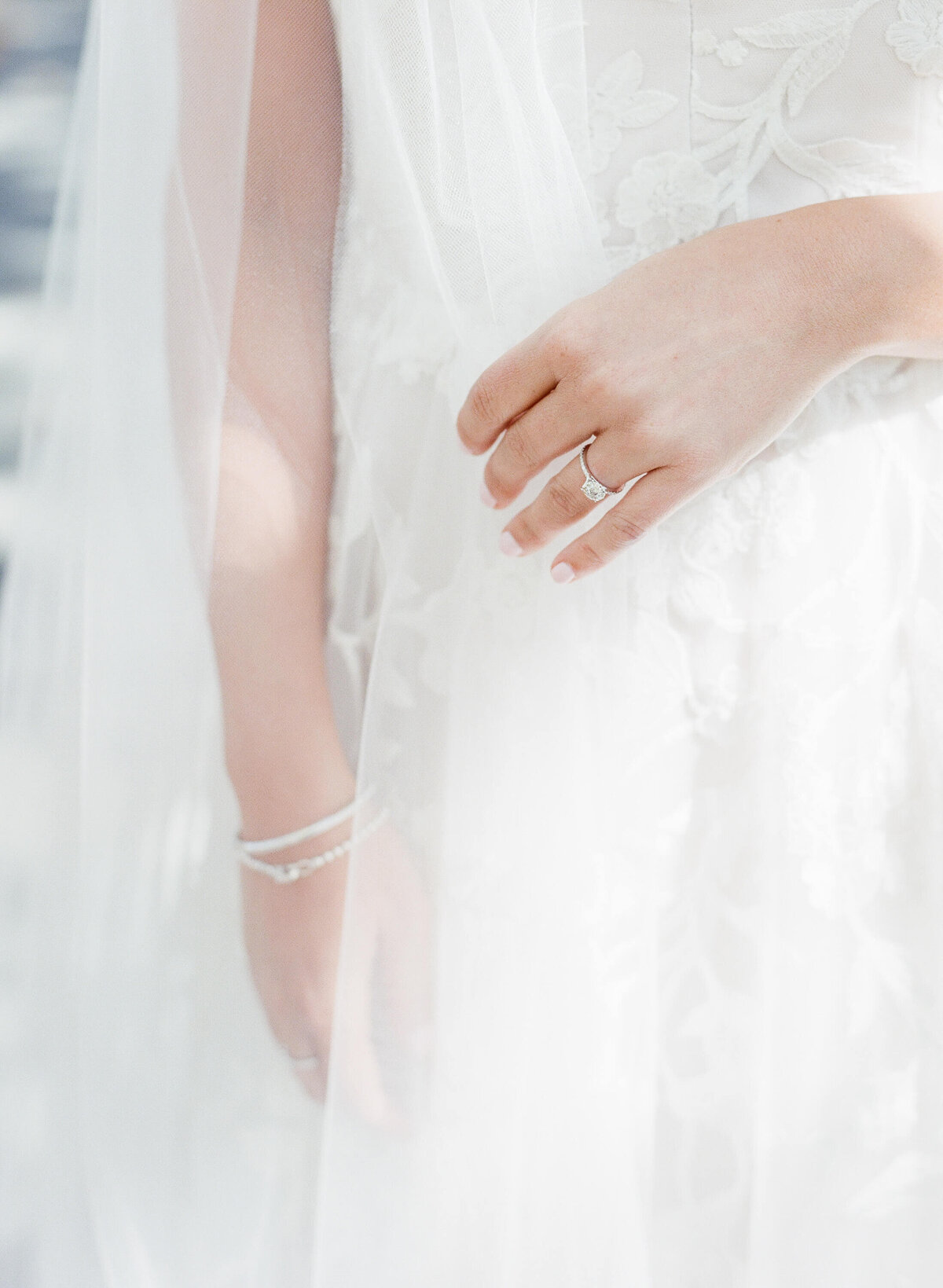 Lucky bride displays her wedding ring in front of her white wedding gown.