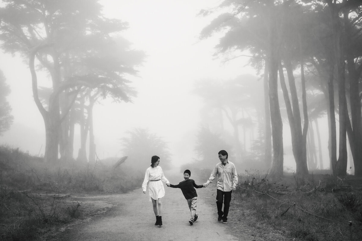 Family walks together on tree lined path at Lands End in San Francisco on a very foggy day