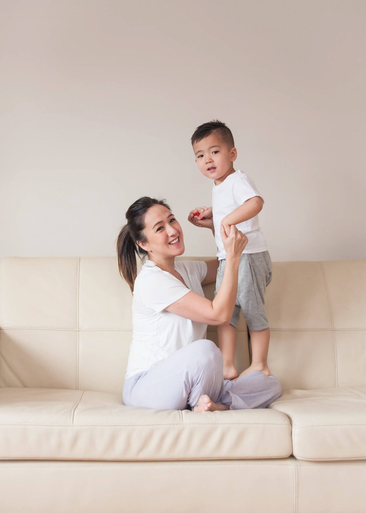 little boy standing on mom's lap on beige couch in lifestyle family session