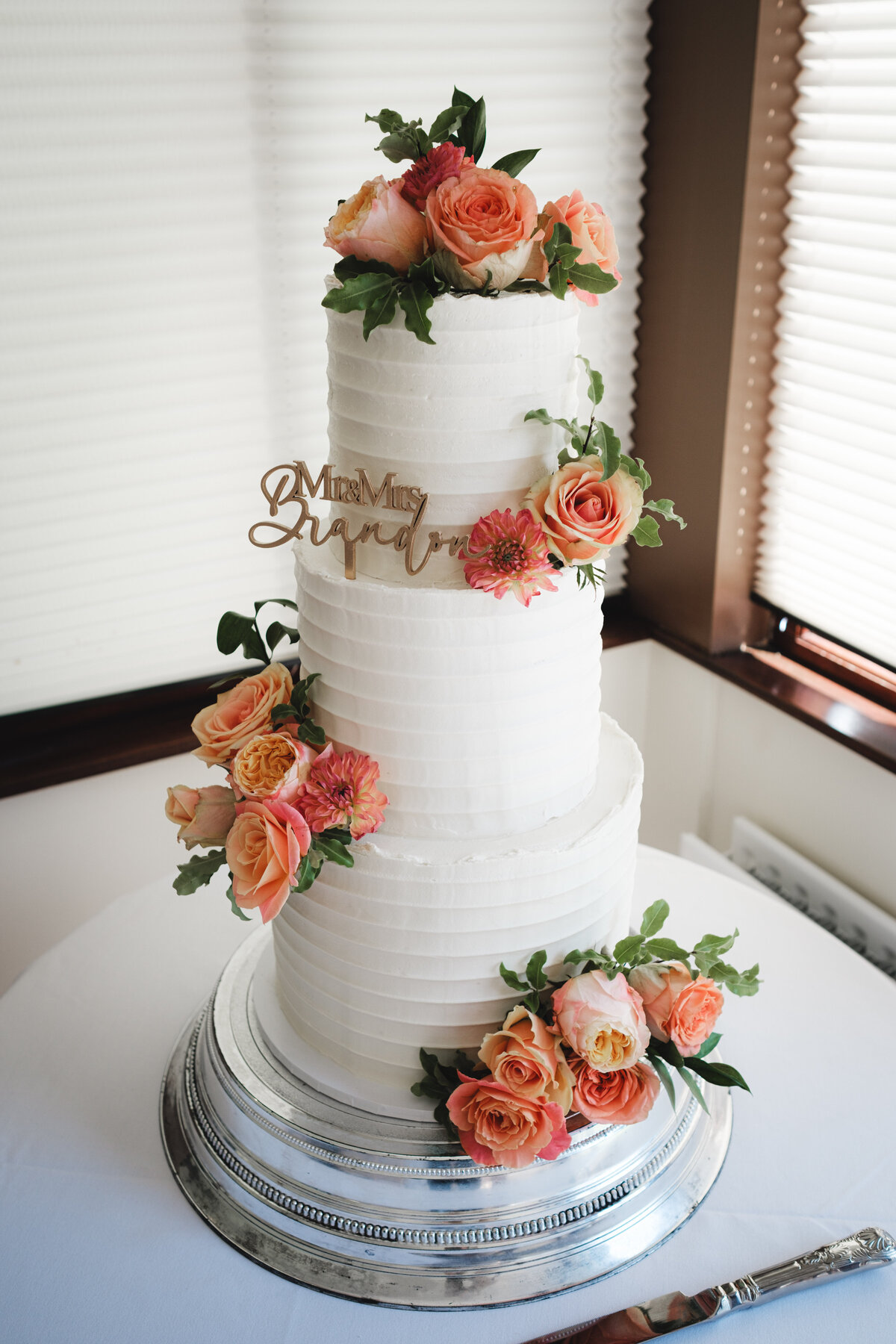 Textured buttercream wedding cake with peach and coral flowes and cake topper