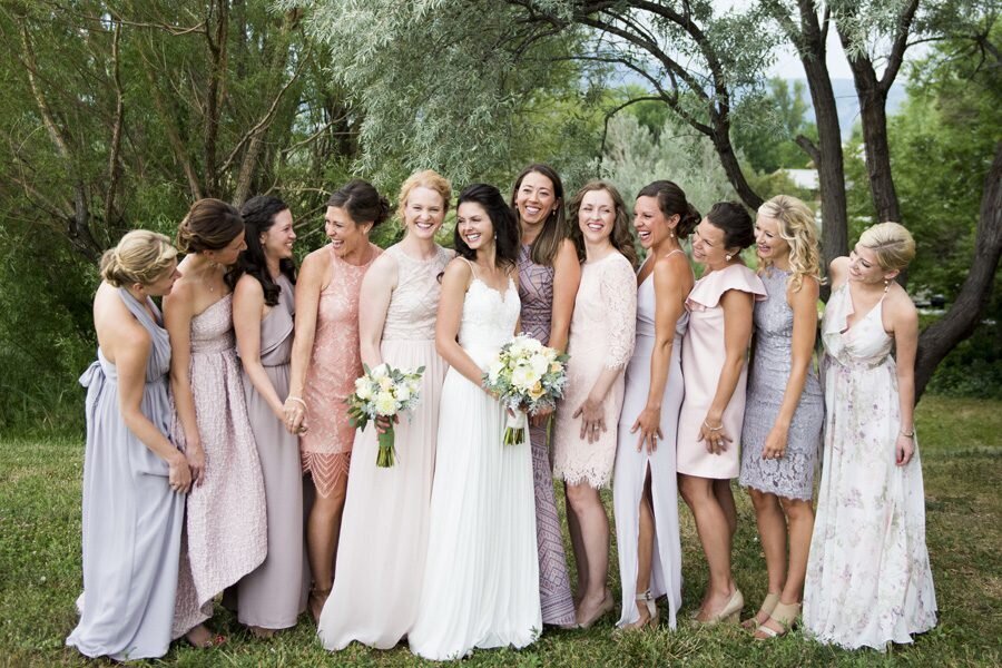 A bride stands with all of her bridesmaids as they all look candidly at one another.