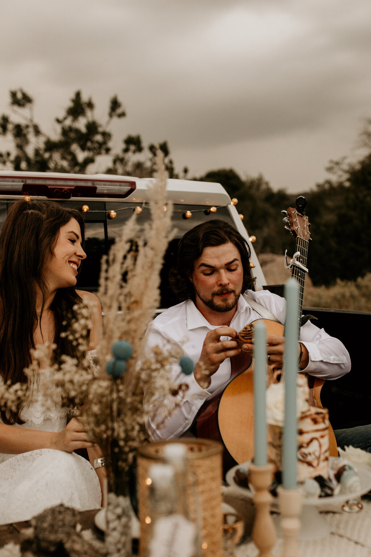 bride and groom eating cake in their truck bed picnic setup
