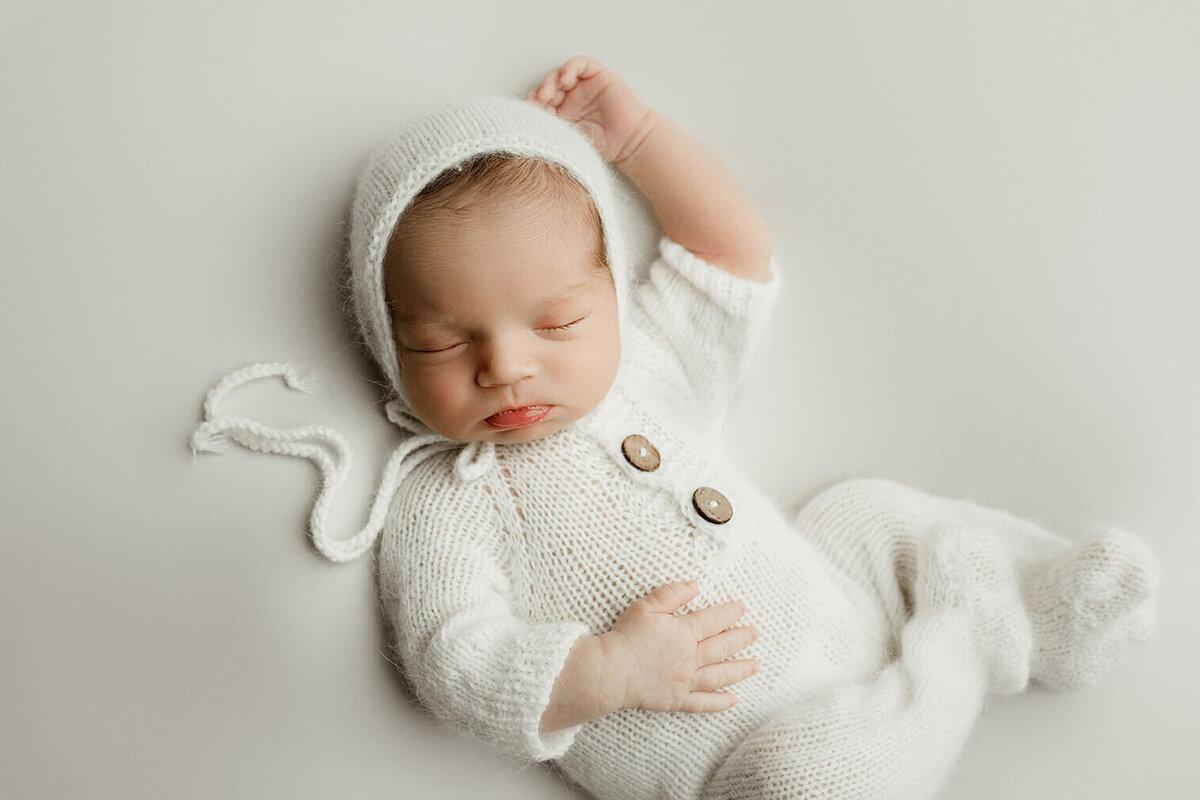Baby sleeping on back in a white knitted romper