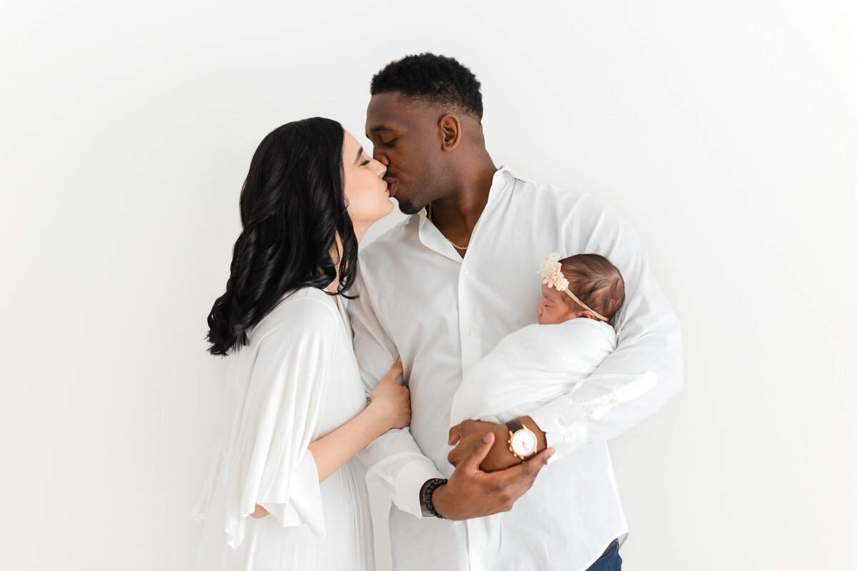 New parents kissing while holding their baby girl in their arms by Virginia Newborn Photographer