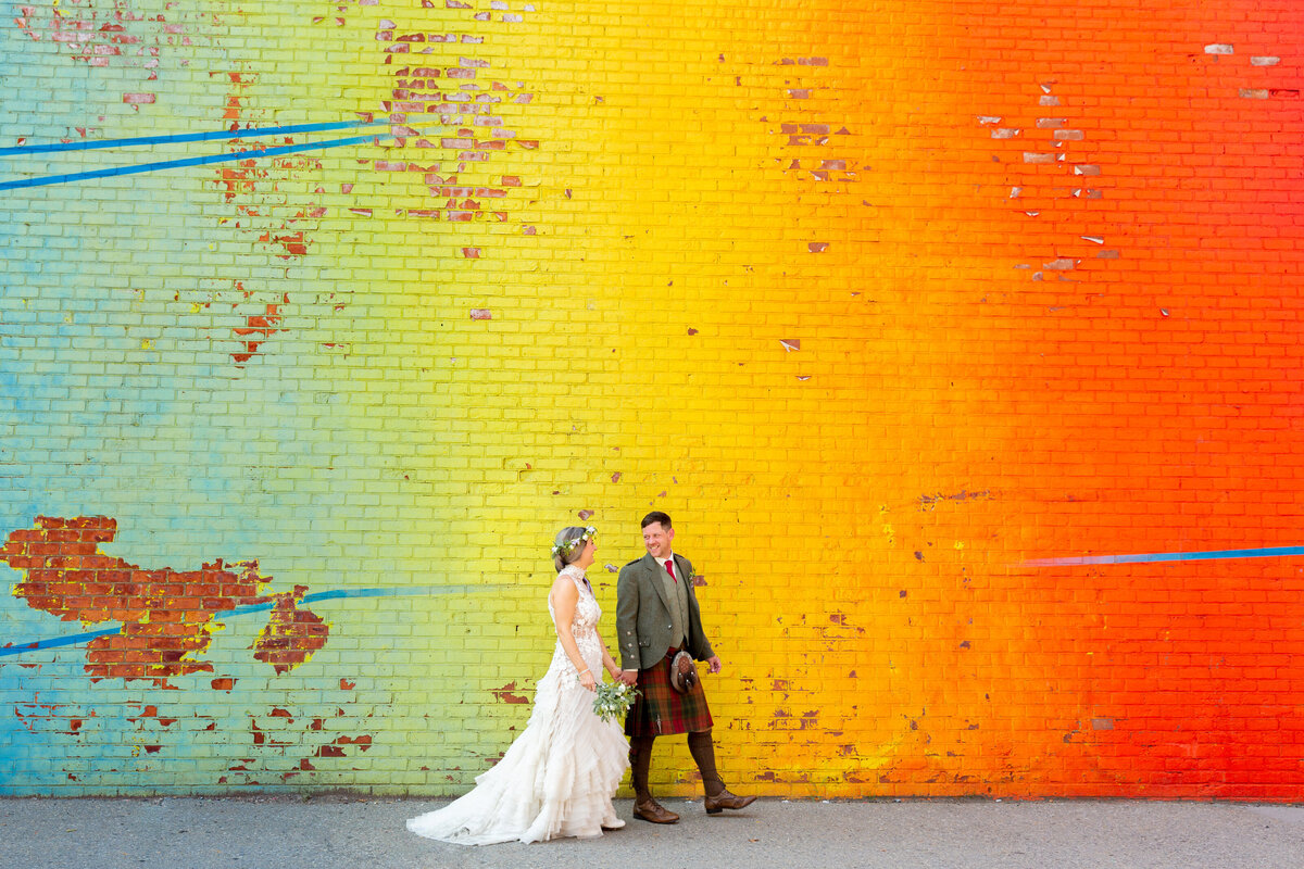 A wedding couple walking along a colorful wall.