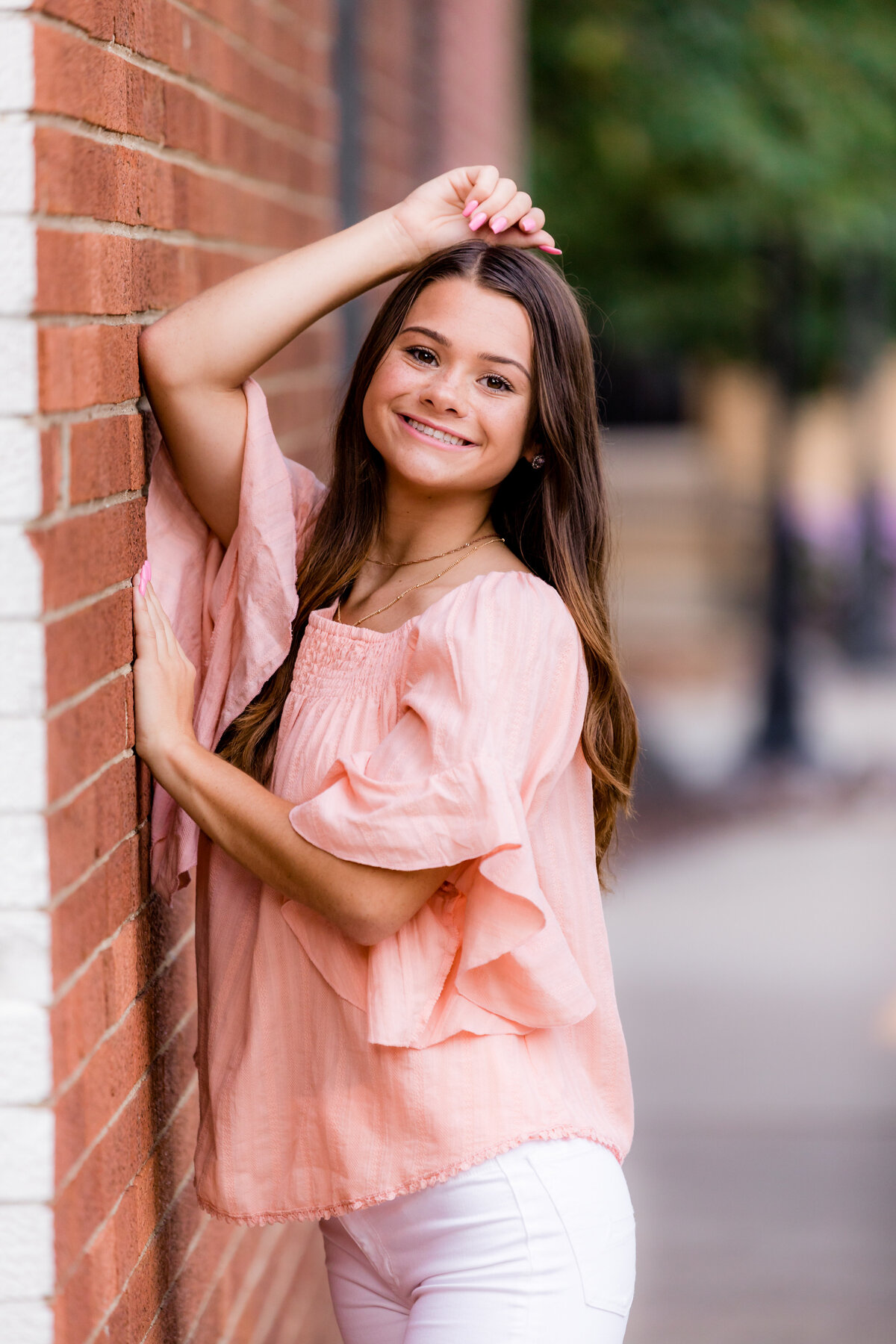 A brunette leans on a brick wall for senior photos.