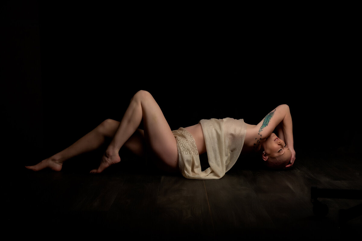 Bald woman posing with a champagne sheet draped across her nude body for her rhode island boudoir photographer