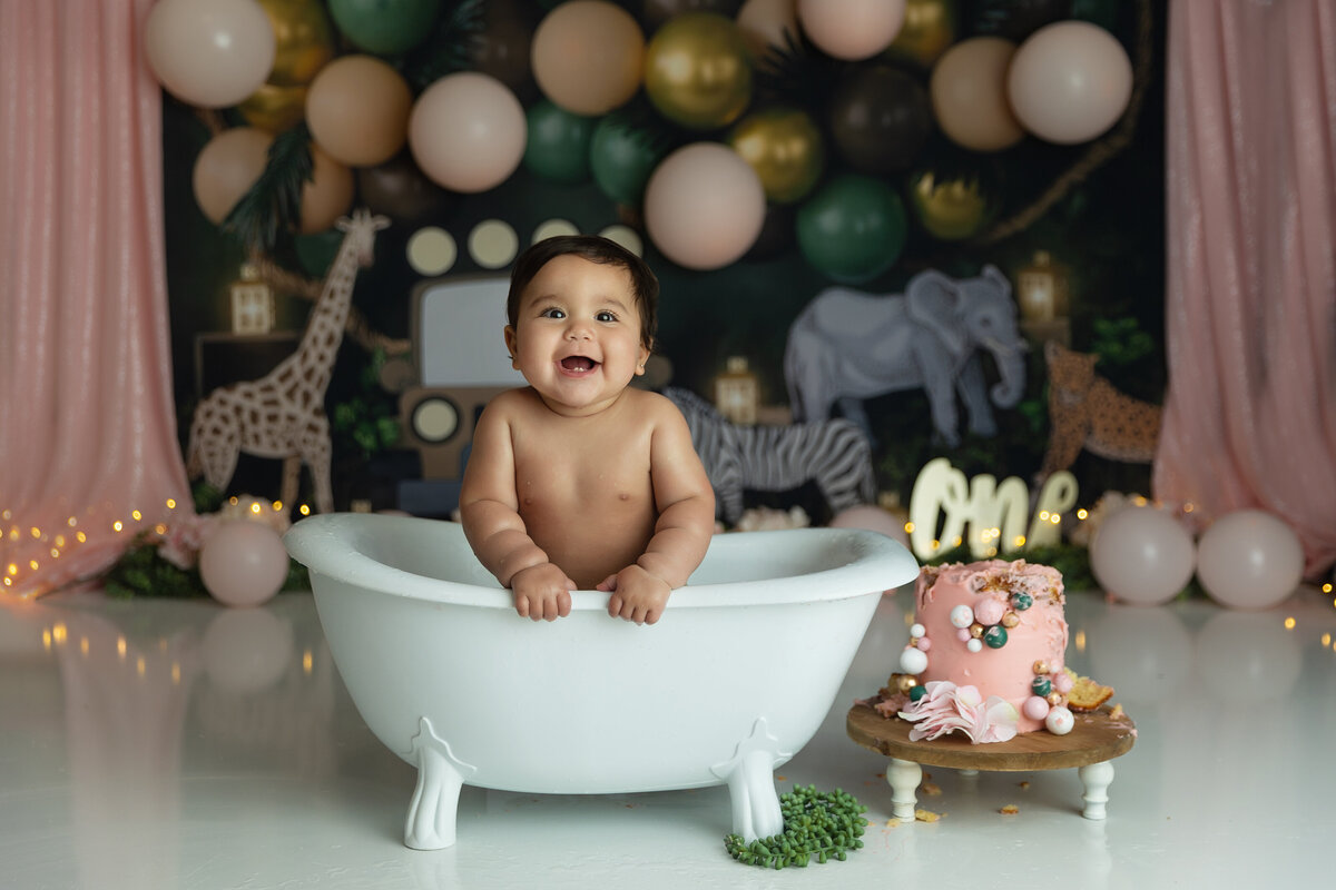 A one year old girl happily plays in a bathtub after cleaning up from eating cake by herself for the first time