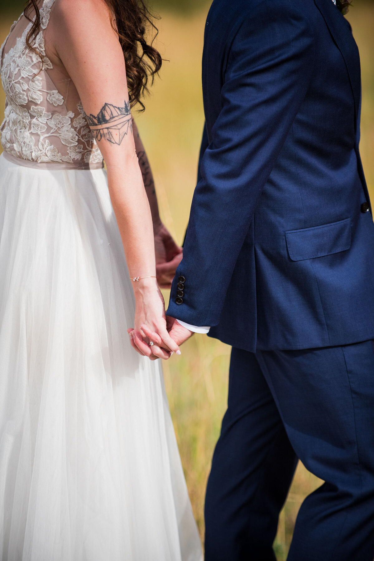 A close up shot of a bride and groom standing back to back holding hands.