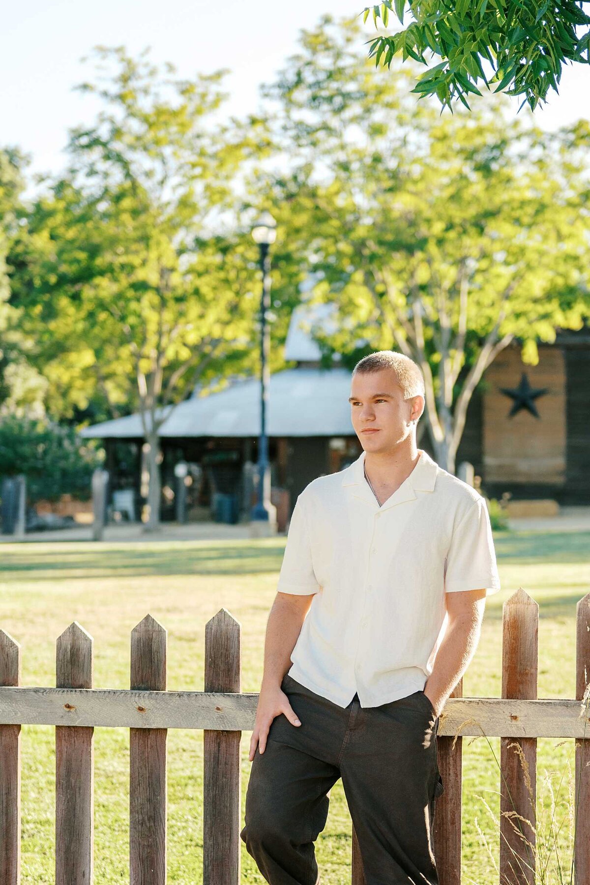 Teen boy in a white shirt and black pants leaning against a fence for his senior guy pics