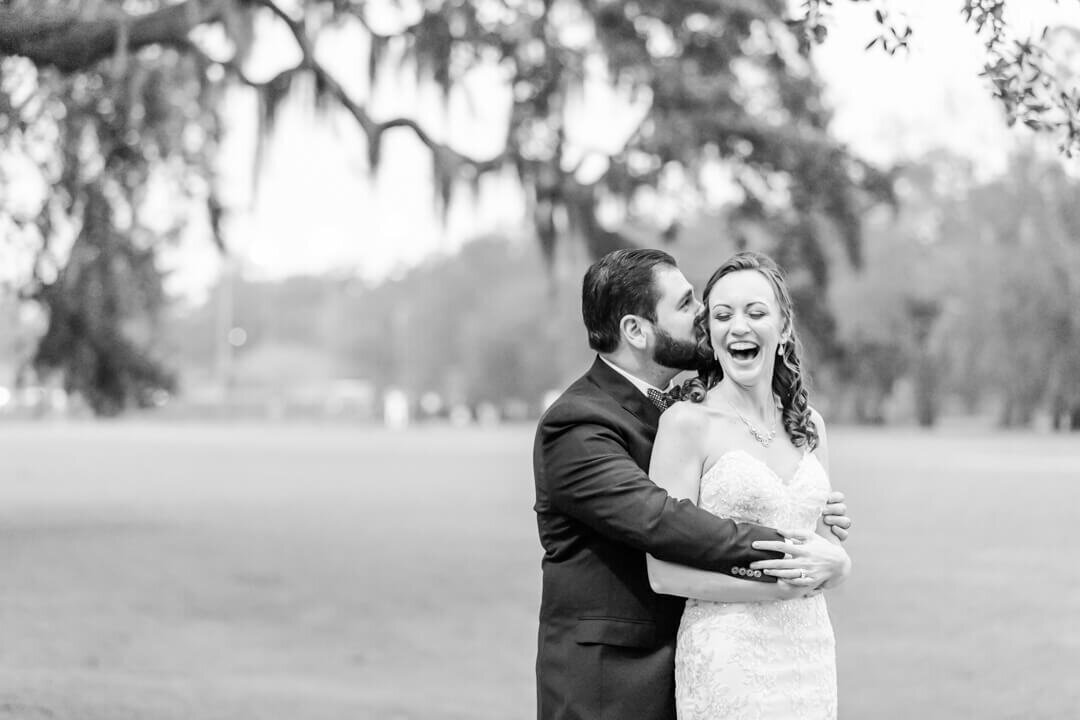 B&W fine art Arkansas wedding photography of a groom whispering in a bride's ear while she laughs.