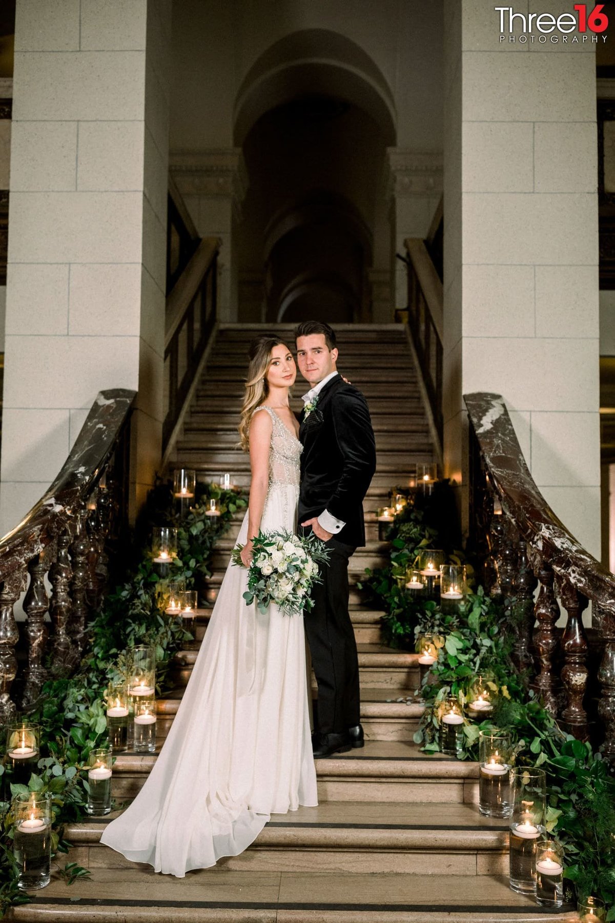 Bride and Groom pose together on the stairs highlighted by candles and plants