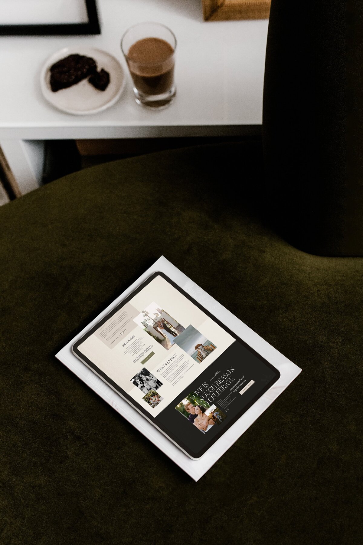 A tablet displaying a website with various articles and images is placed on top of a book with a white cover, both resting on a dark green surface. The website showcases brand and identity services for luxury photographers.