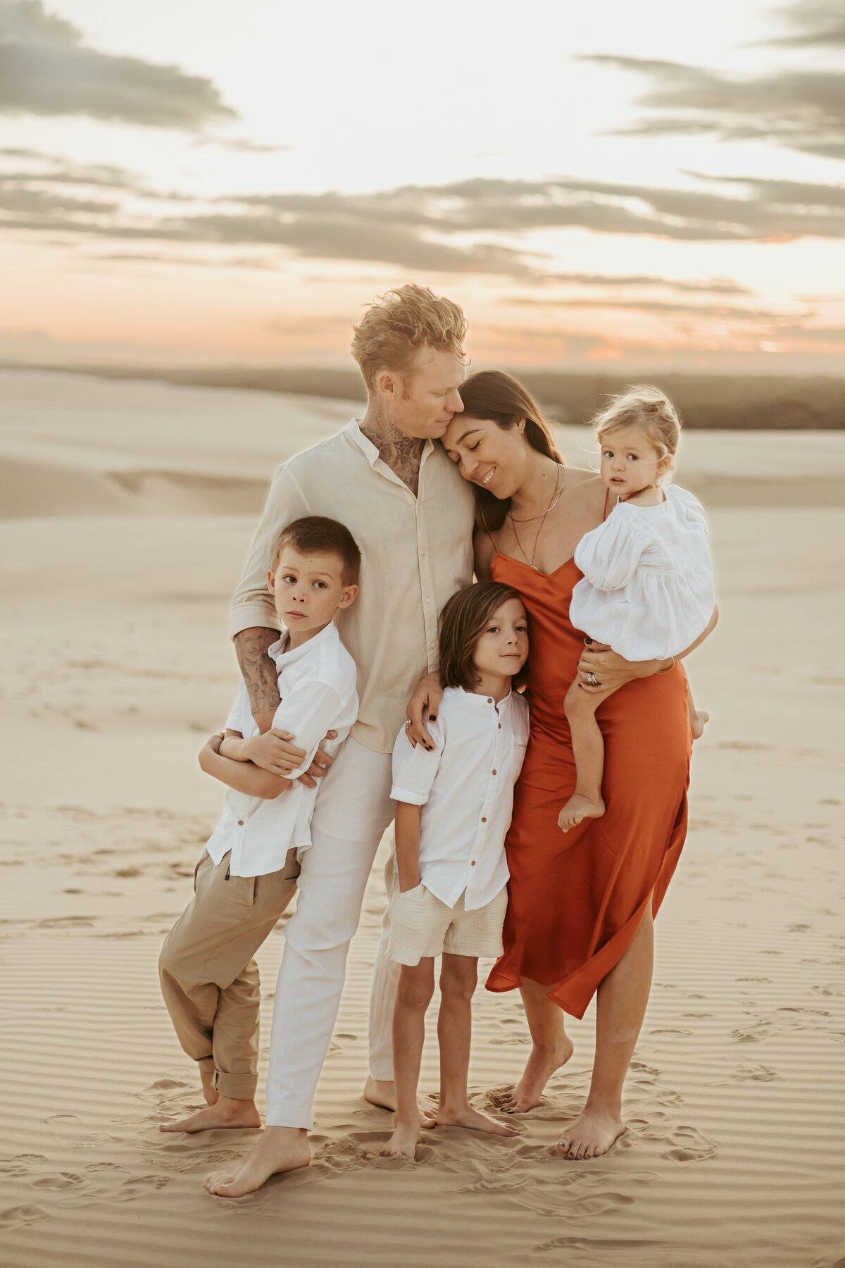 Gorgeous Sydney family of five posing together on the sand at sunset.