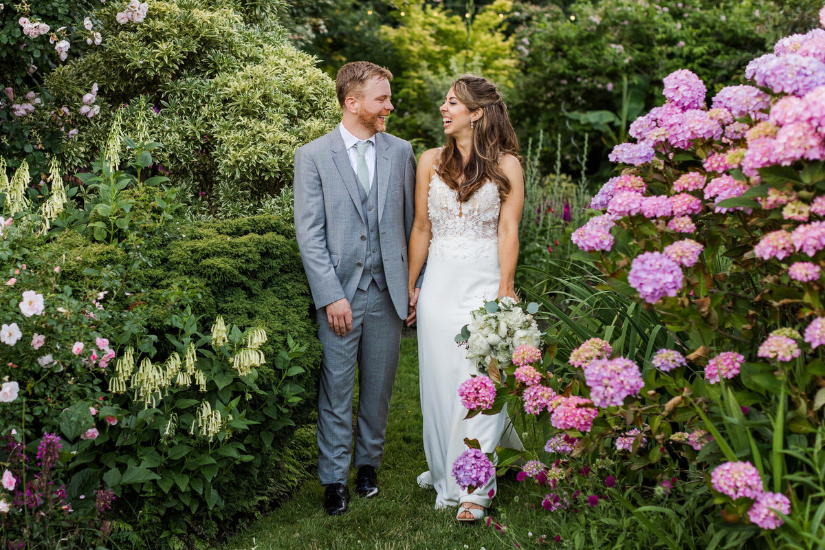 Laughing-bride-and-groom-walk-through-colorful-flower-gardens-at-Froggsong-venue-at-Vashon-Island-WA-by-Joanna-Monger-Photography