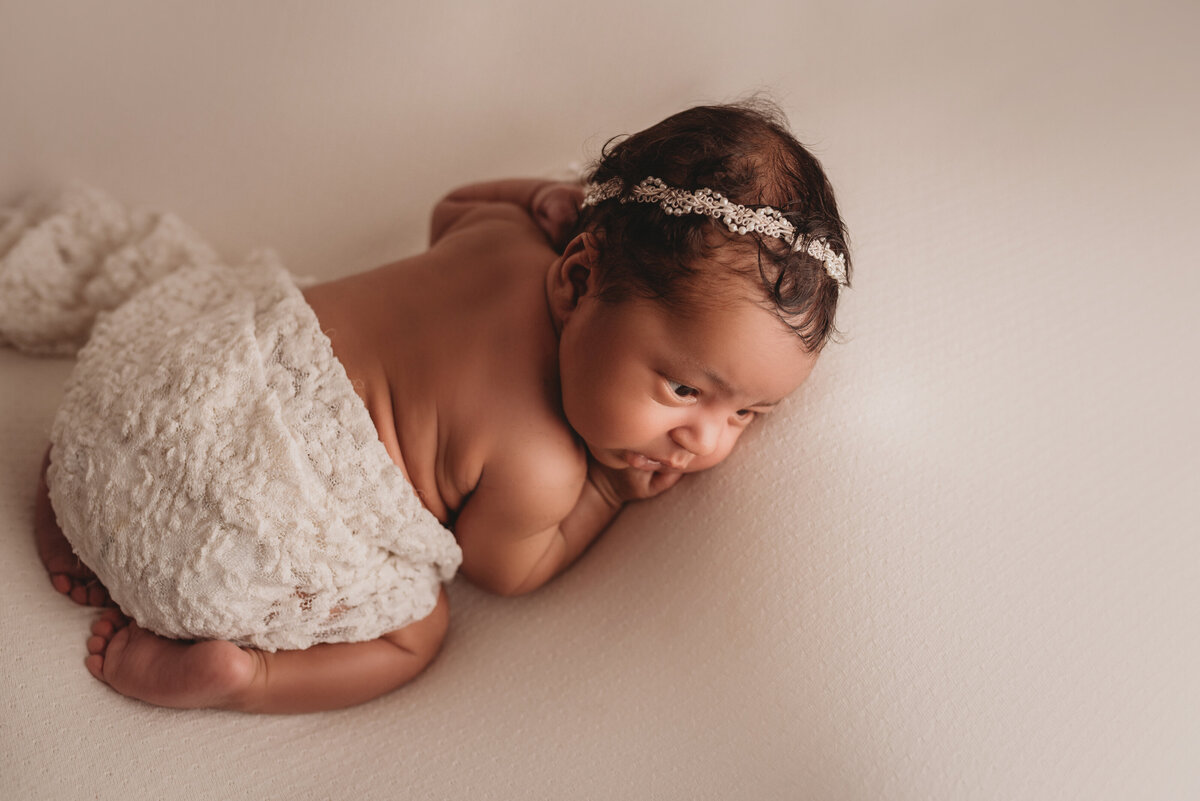 Newborn baby girl at Atlanta, GA newborn portrait studio posing in lace and creams on her tummy