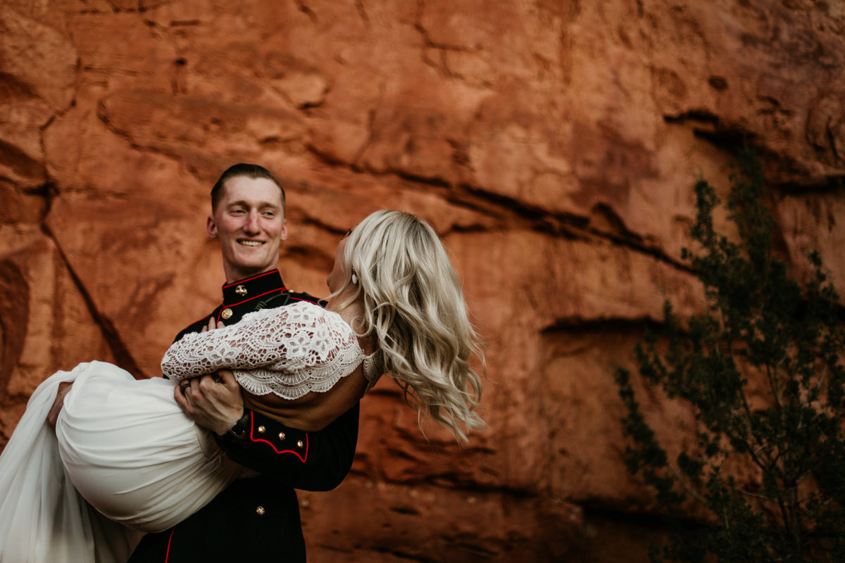 groom carrying new wife by red rocks