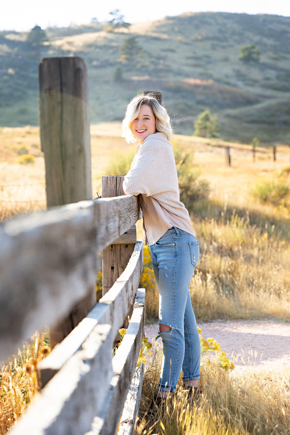 Blonde high school senior leans on a wood farm fence