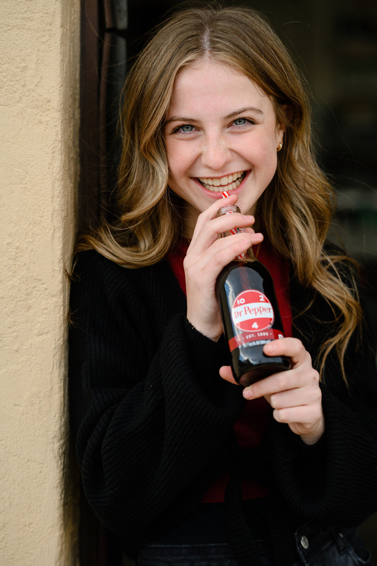Denver senior Photographer captures a young girl smiling at the camera while drinking a glass bottle of dr pepper