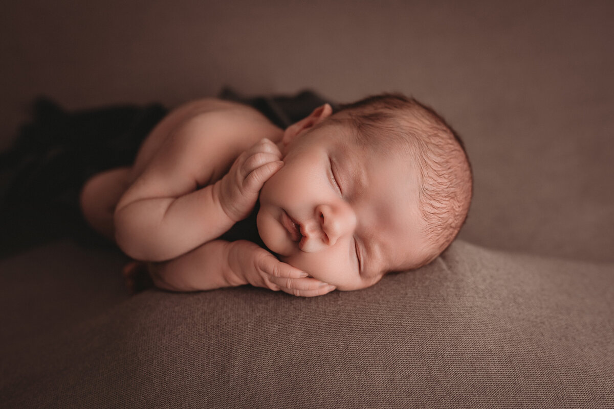 atlanta newborn photographer capturing 2 week old baby boy at his newborn photography session asleep with hands under cheek laying on side swaddled in cream fabric