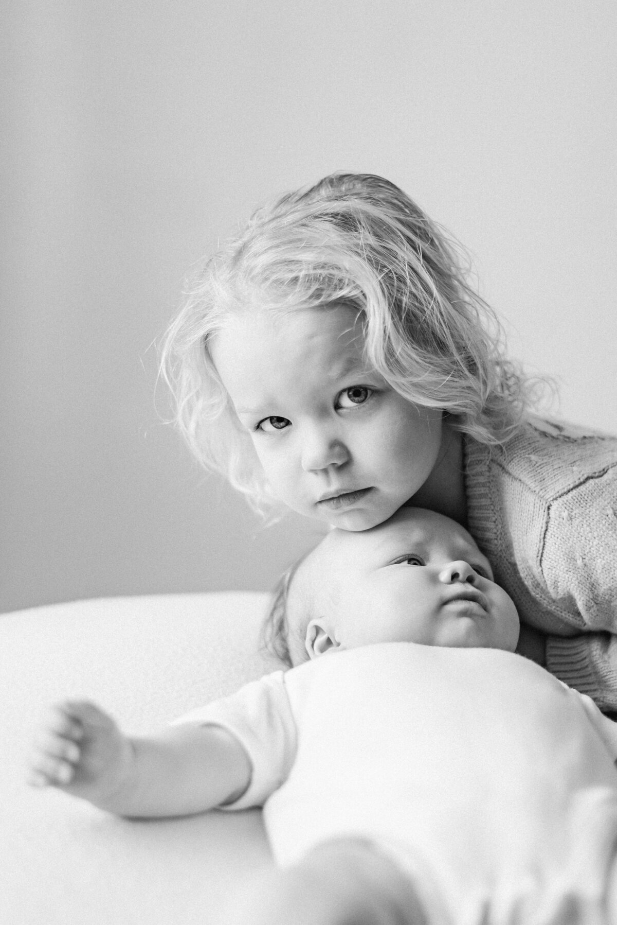 Sister leaning over baby girl at milestone photoshoot in Billingshurst
