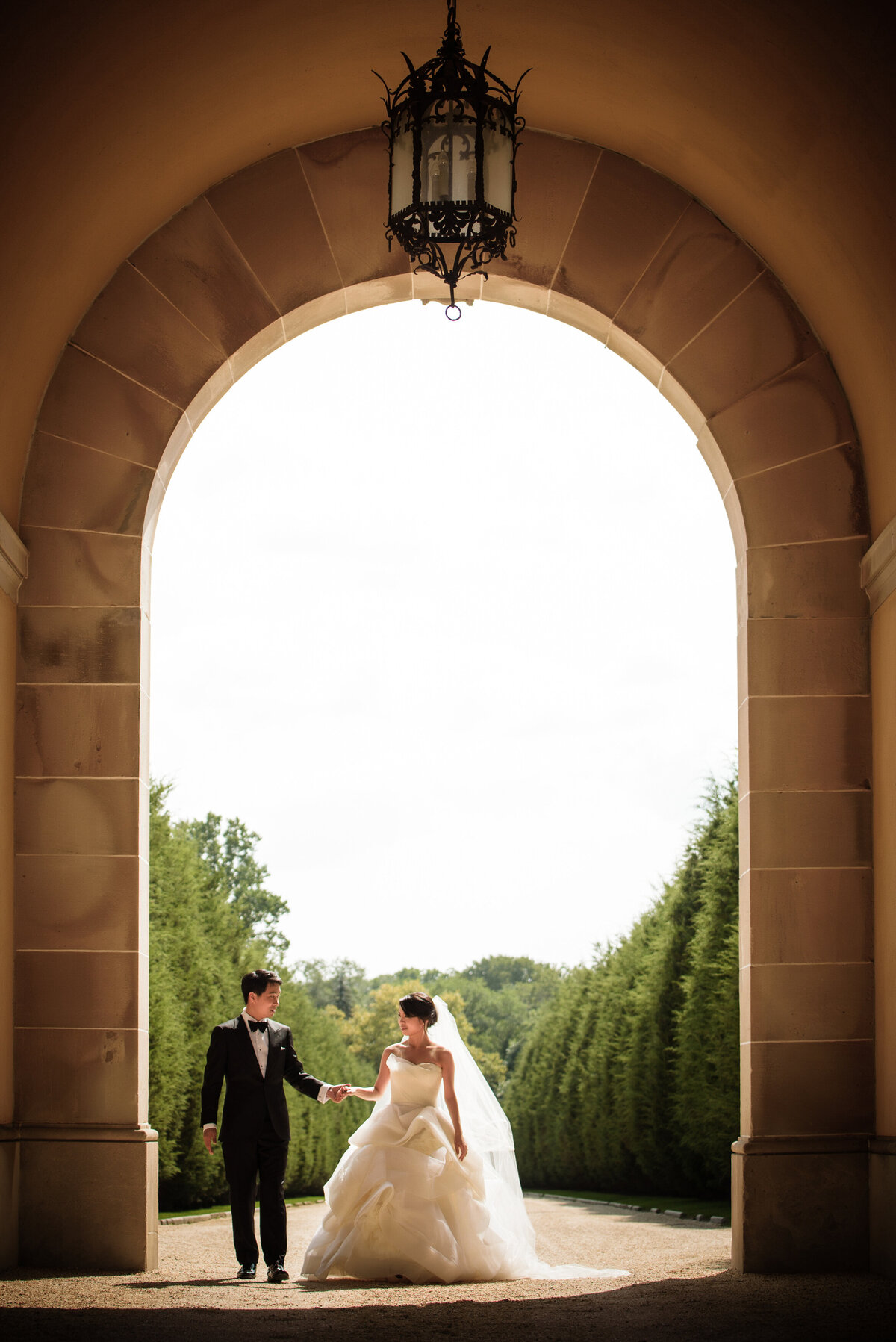 A bride and groom walking along a gravel path while holding hands.