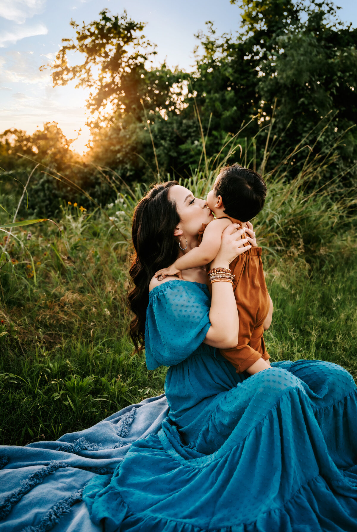 Family Photographer, a mother kisses her baby in a lush grassy landscape