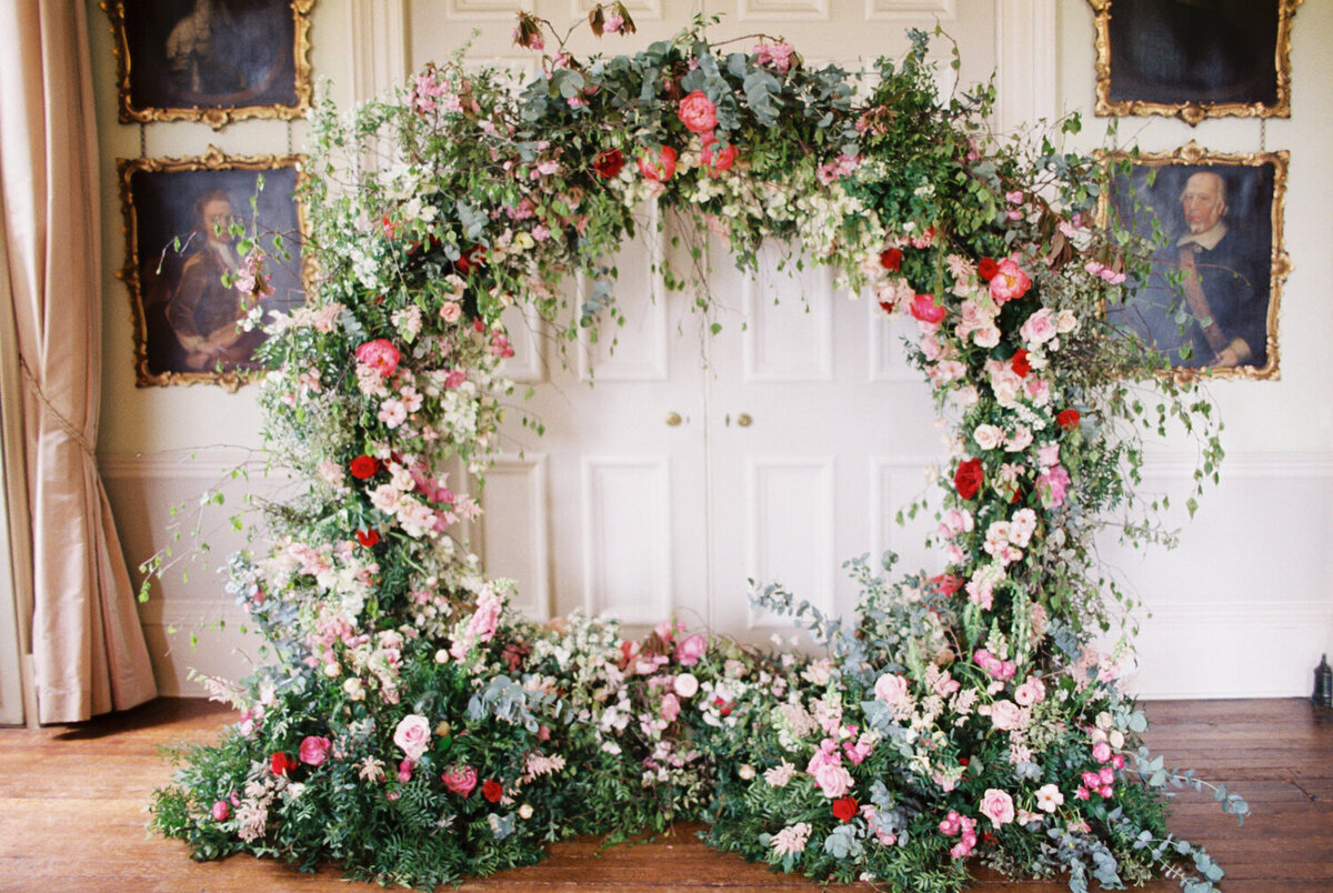 large round circle wedding arch made with fresh bold red and blush flowers and lots of greenery